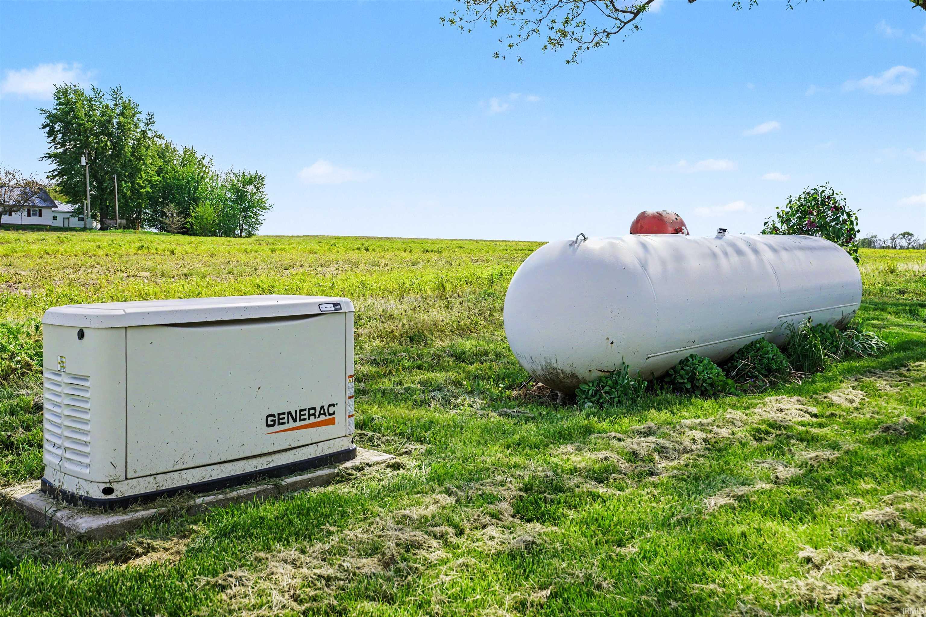 Generac whole-home generator on a concrete pad, accompanied by a large, white propane tank