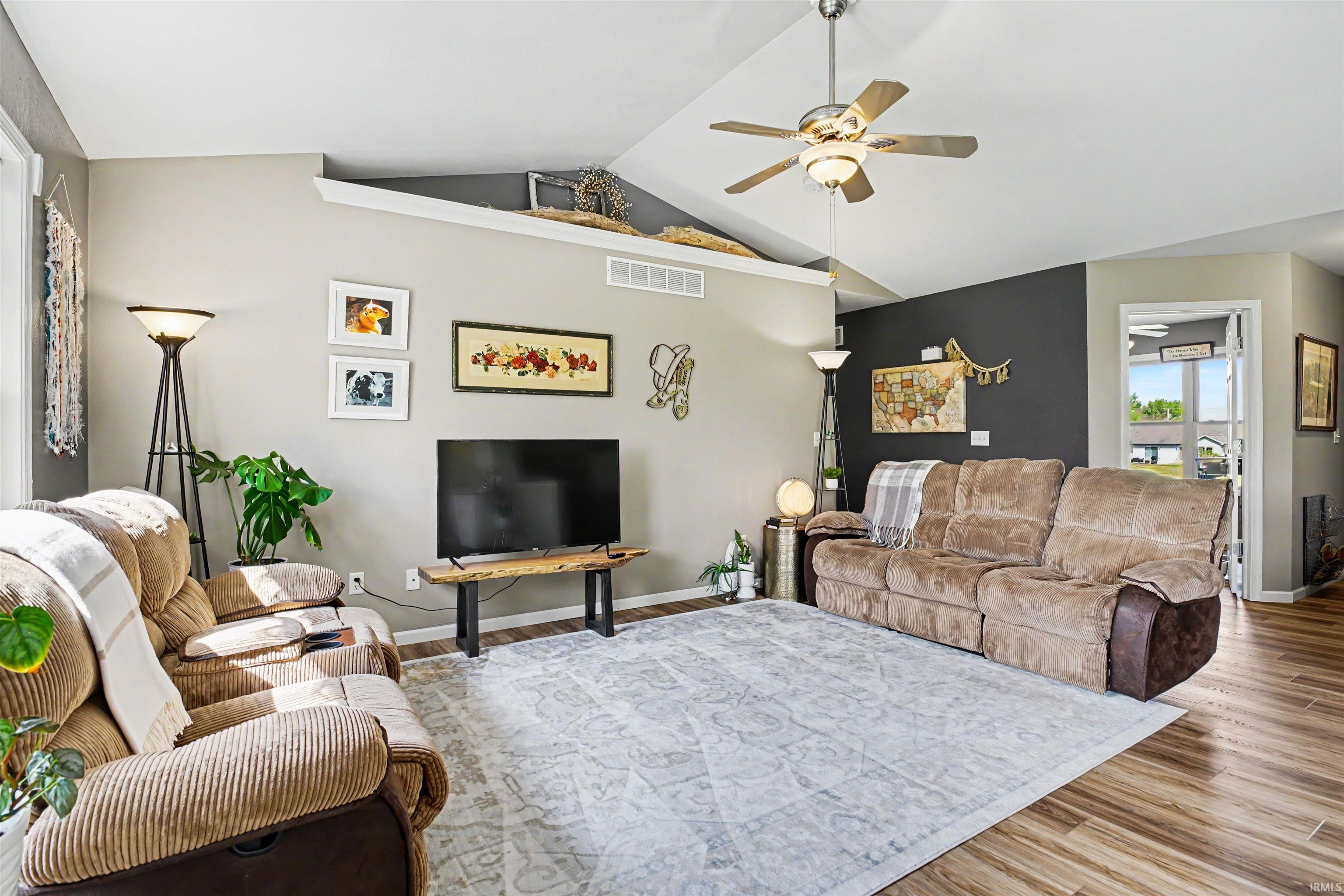 Expansive living area featuring vaulted ceilings, wood-finish flooring, a ceiling fan with integrated lighting, and a built-in display ledge
