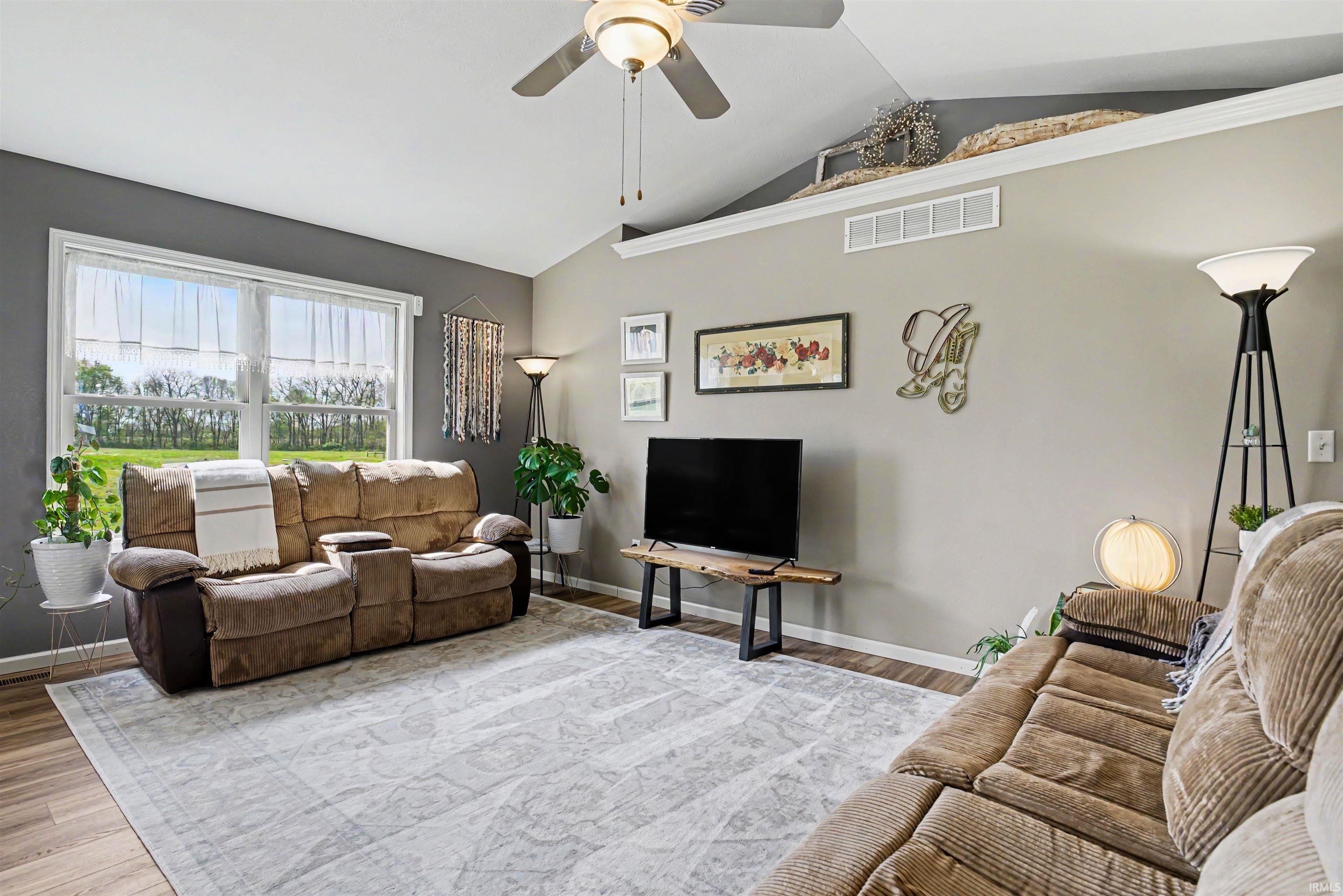 Spacious living area featuring vaulted ceilings, wood-finish flooring, and a ceiling fan with integrated lighting