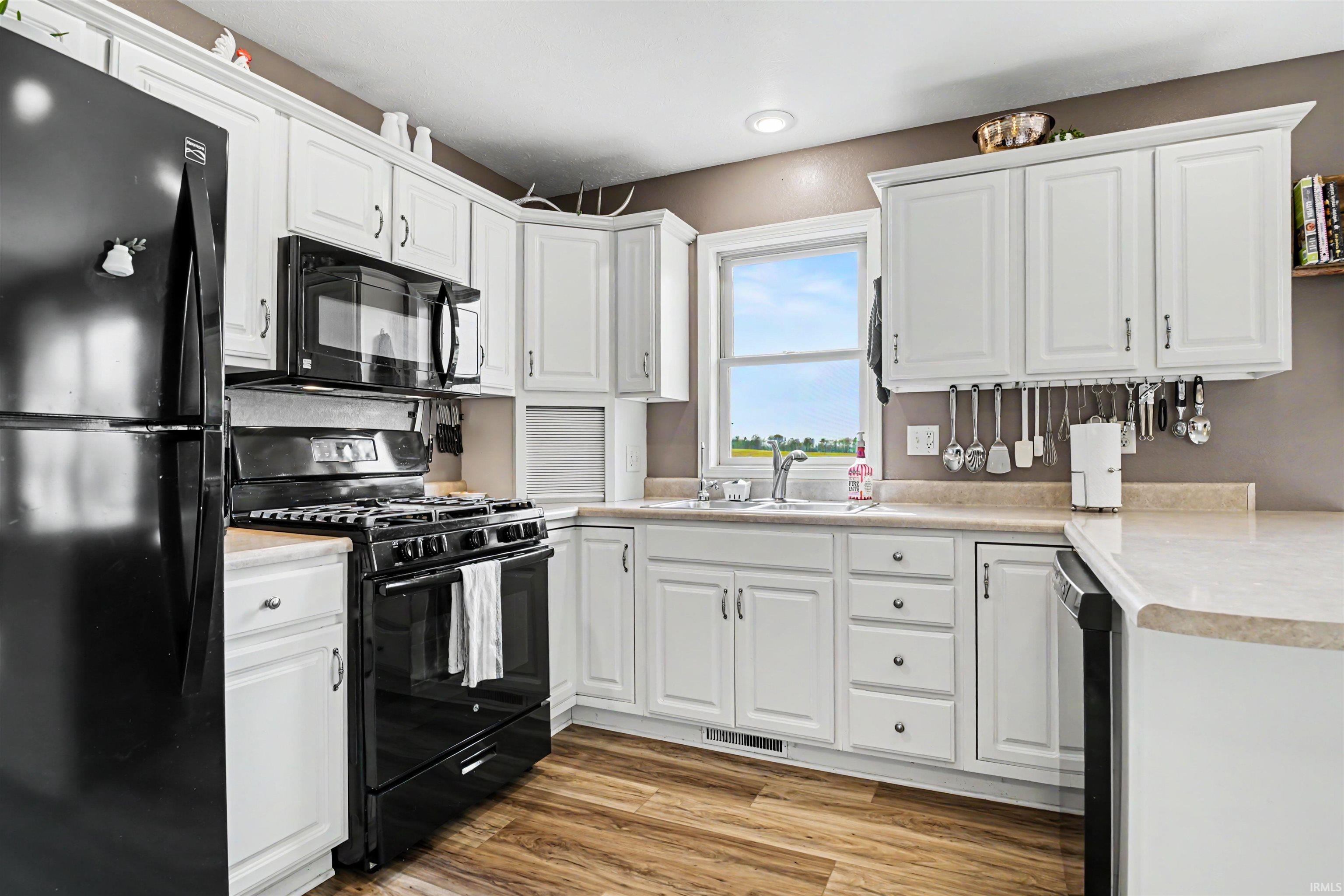 Kitchen featuring white cabinetry, black appliances, light-toned countertops, and wood-finish flooring