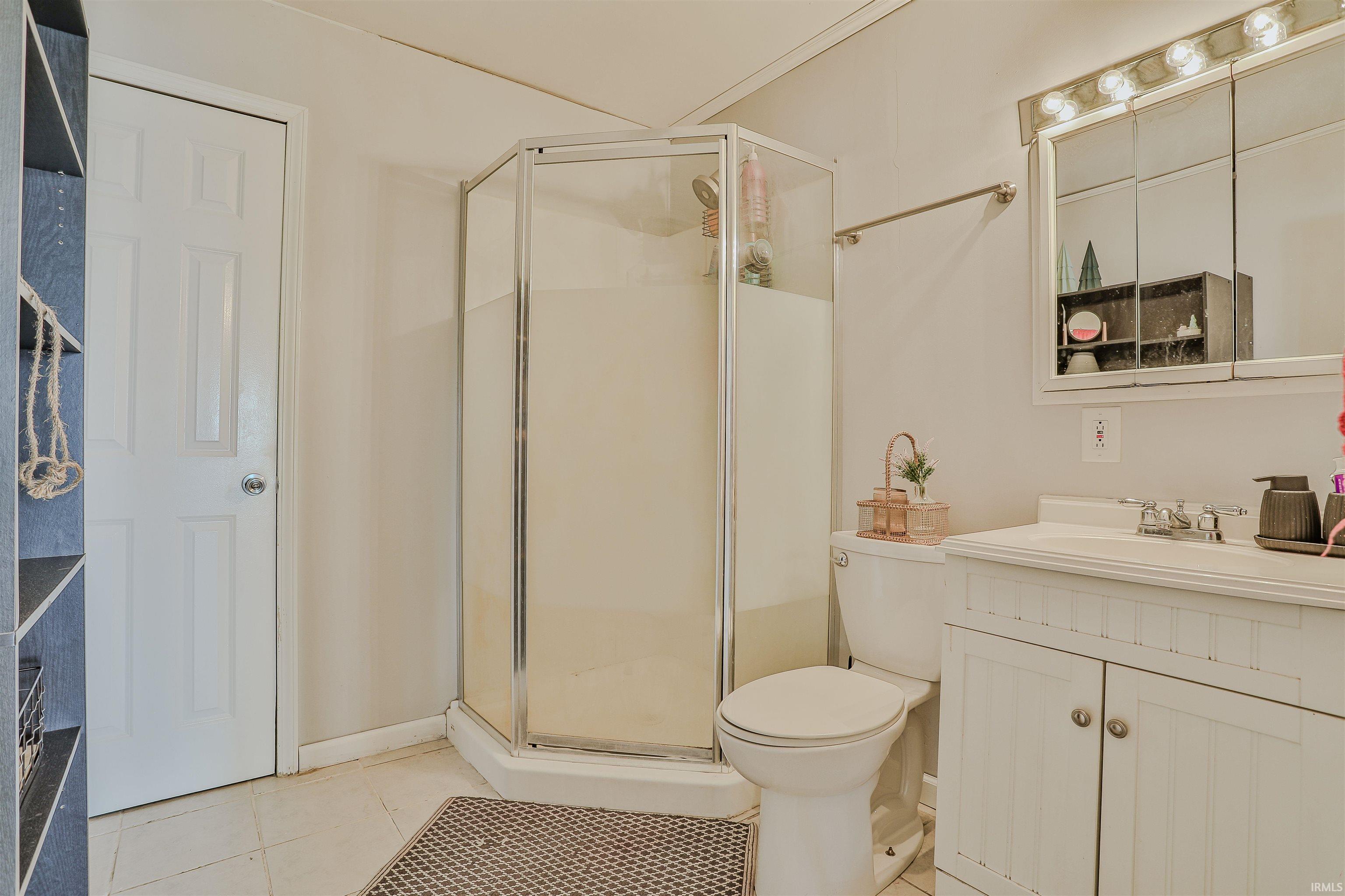 Bathroom featuring a corner shower enclosure, white panel vanity with integrated sink, mirrored medicine cabinet with vanity lighting, and tiled flooring