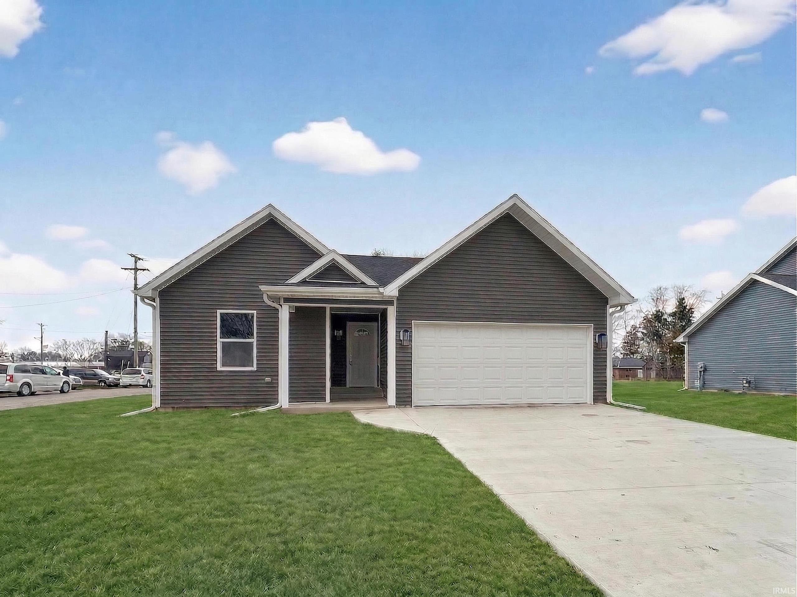 Contemporary single-story residence featuring dark siding, a gabled roofline, an attached garage with a white door, a concrete driveway, and a front lawn
