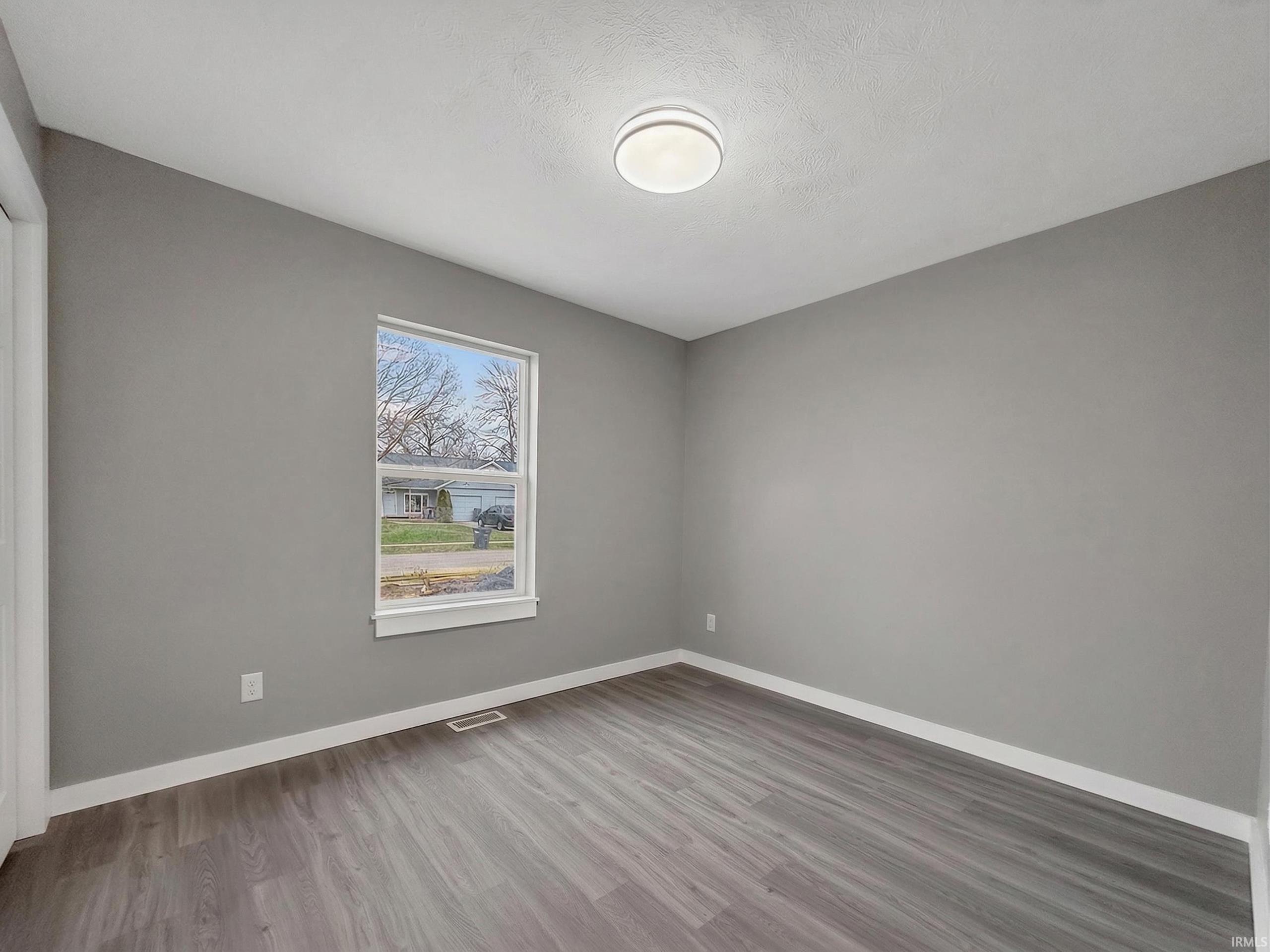 Room featuring wood-finish flooring, a single window, and a ceiling-mounted light fixture