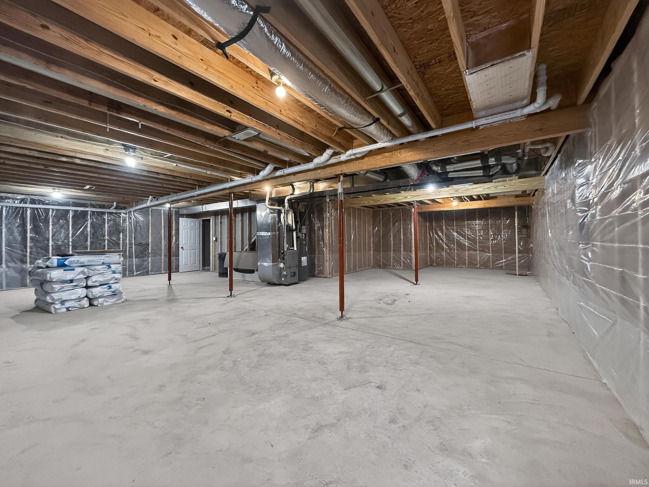 Expansive unfinished basement featuring a concrete floor, exposed wood ceiling joists, and visible utility infrastructure