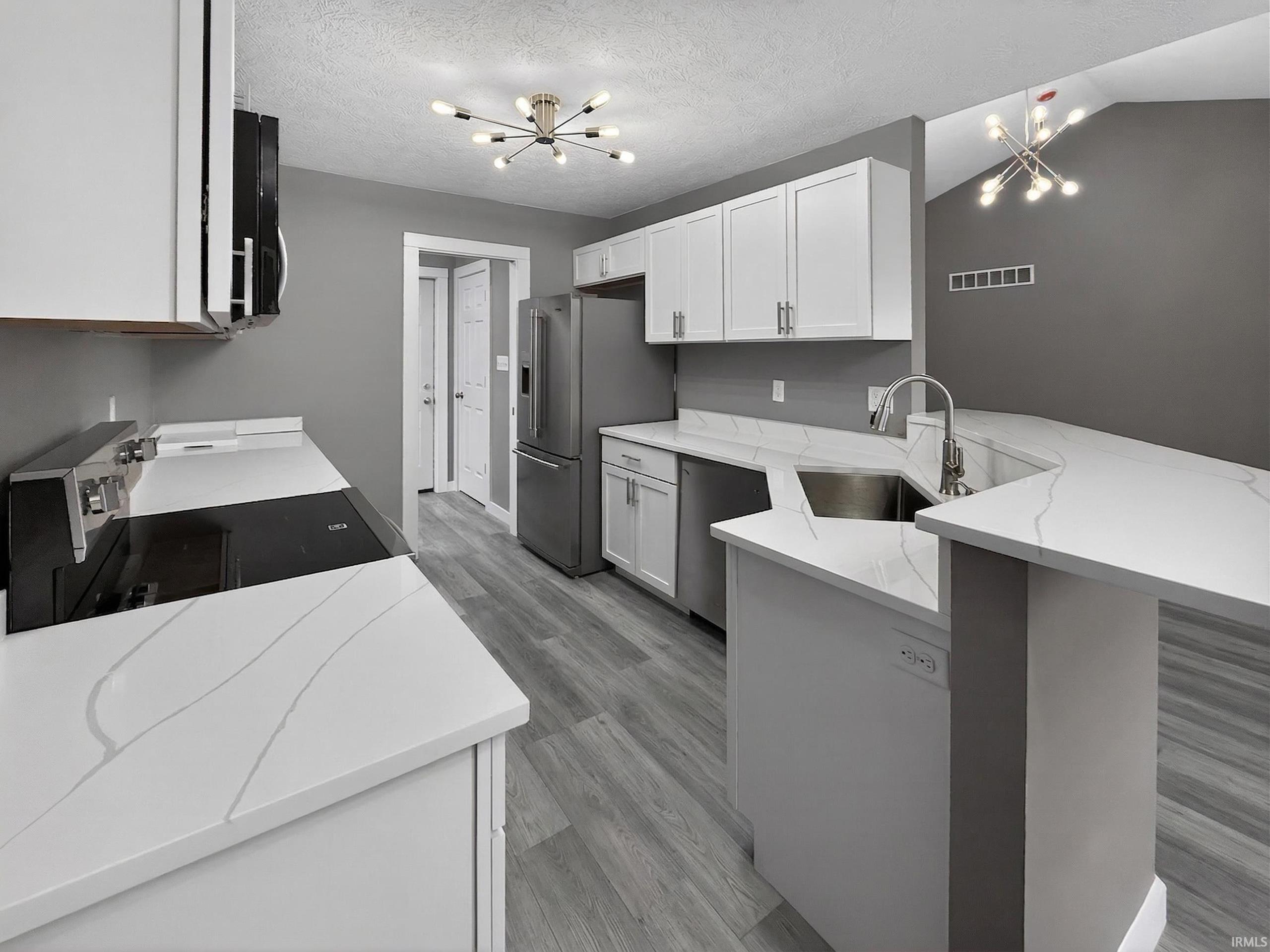 Kitchen featuring white cabinetry, stainless steel appliances, wood-finish flooring, white countertops with veining, and modern light fixtures
