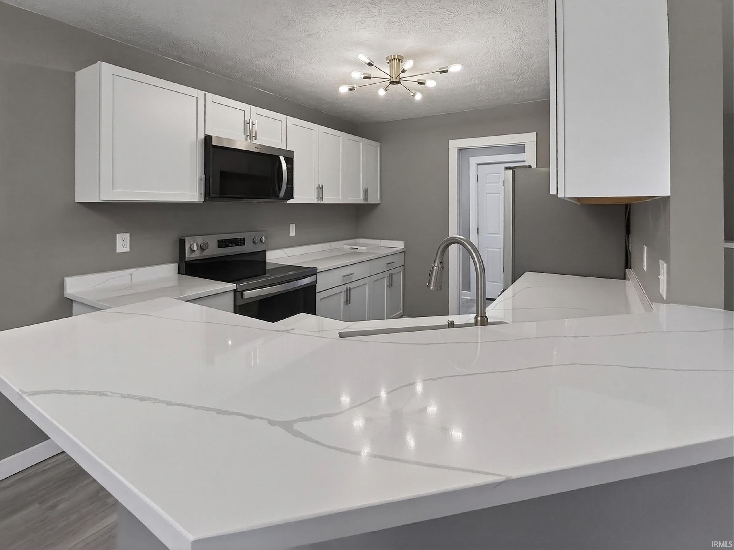 Kitchen featuring white shaker cabinetry, stainless steel appliances, light-toned countertops with veining, and a contemporary ceiling fixture
