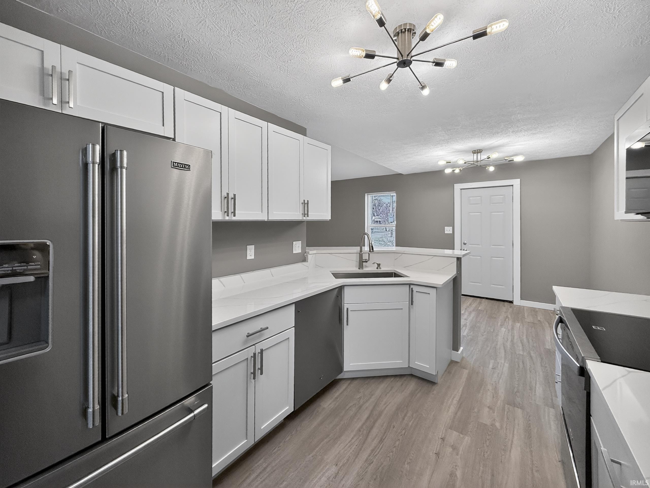 Modern kitchen featuring stainless steel appliances, white shaker cabinetry, light-toned countertops, and wood-finish flooring