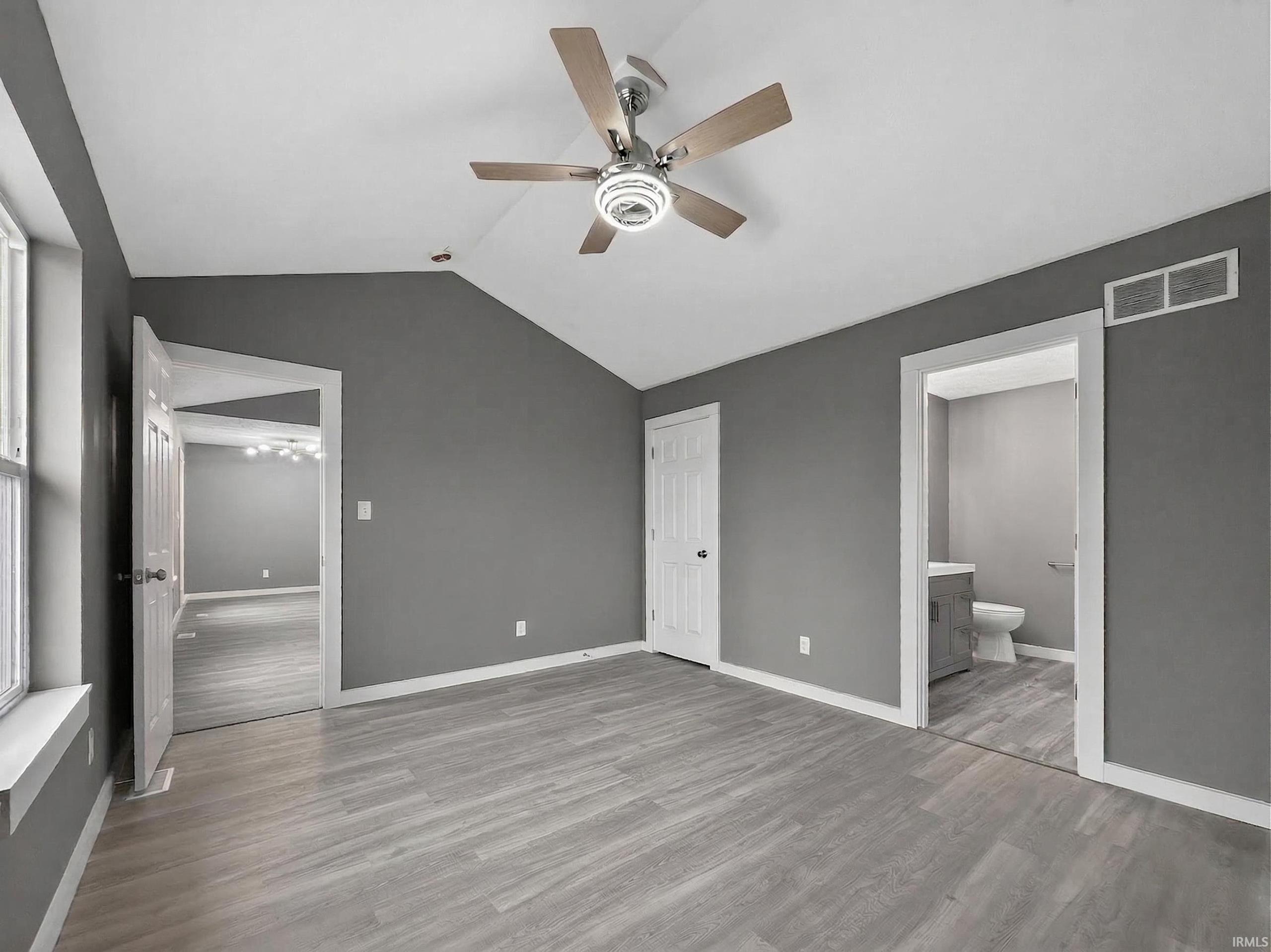 Spacious room featuring vaulted ceilings, wood-finish flooring, a modern ceiling fan with integrated lighting, and a white interior door