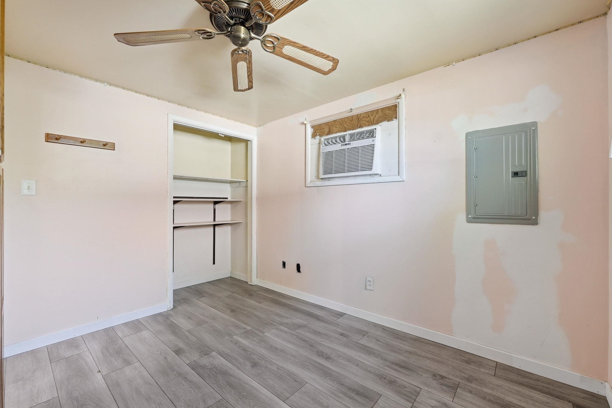 Interior space featuring wood-finish flooring, a ceiling fan fixture, a window-mounted air conditioning unit, built-in shelving, and a wall-mounted electrical panel