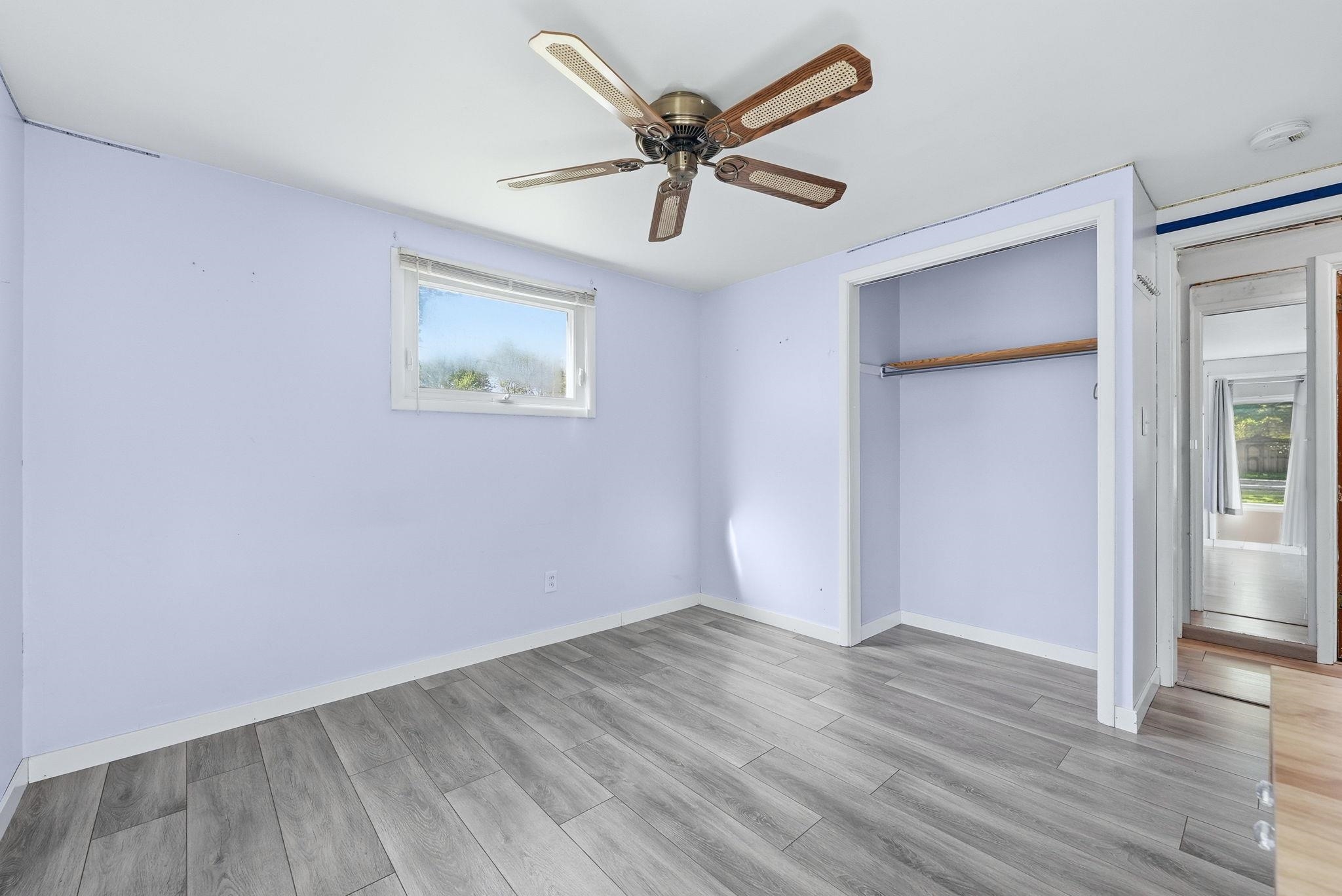 Interior room featuring wood-finish flooring, a ceiling fan with light fixture, a window with a white frame, and an open closet with a hanging rod