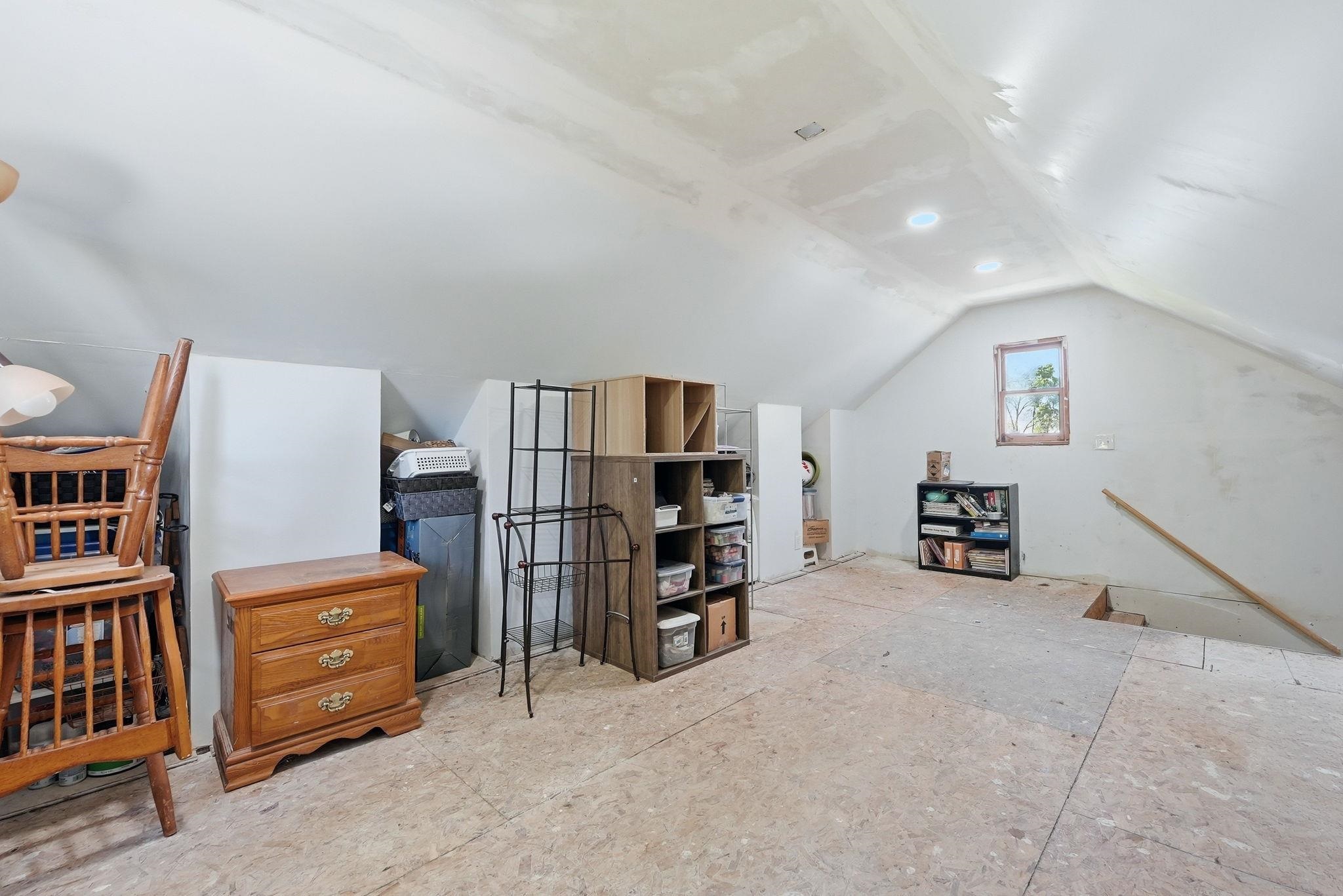 Spacious attic area featuring a sloped ceiling, recessed lighting, and a window with wooden trim