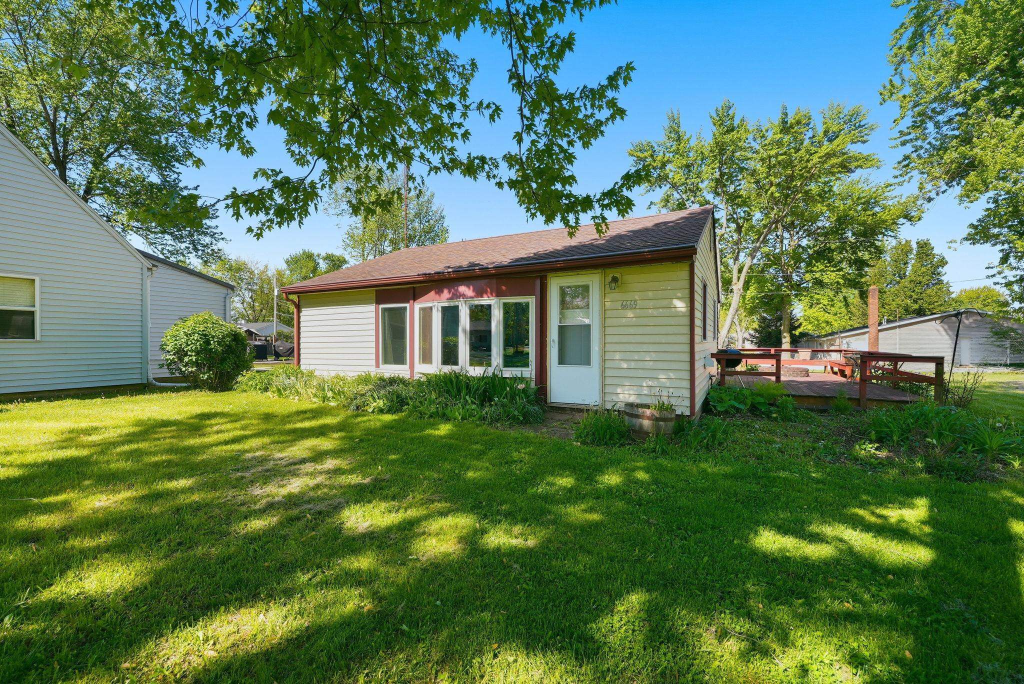 Rear elevation featuring light-colored siding, a contrasting red trim, and a prominent sunroom with multiple windows