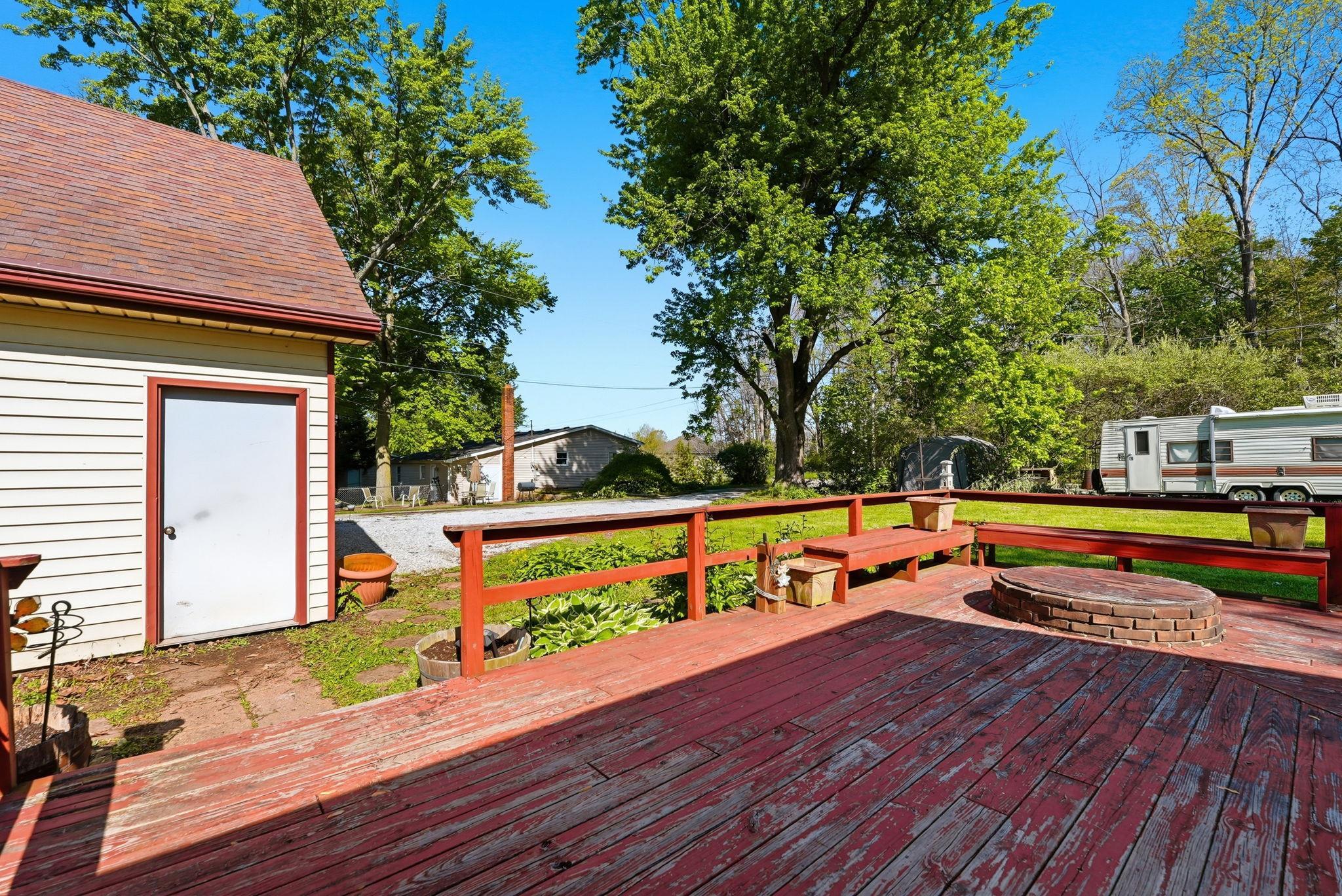 Outdoor wood deck featuring a circular brick fire pit, built-in wood benches, and a red wood railing