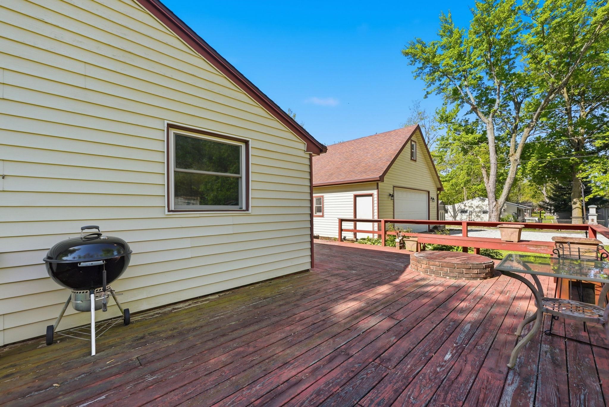 Spacious wood-finish deck with a red-stained surface, featuring a built-in brick fire pit