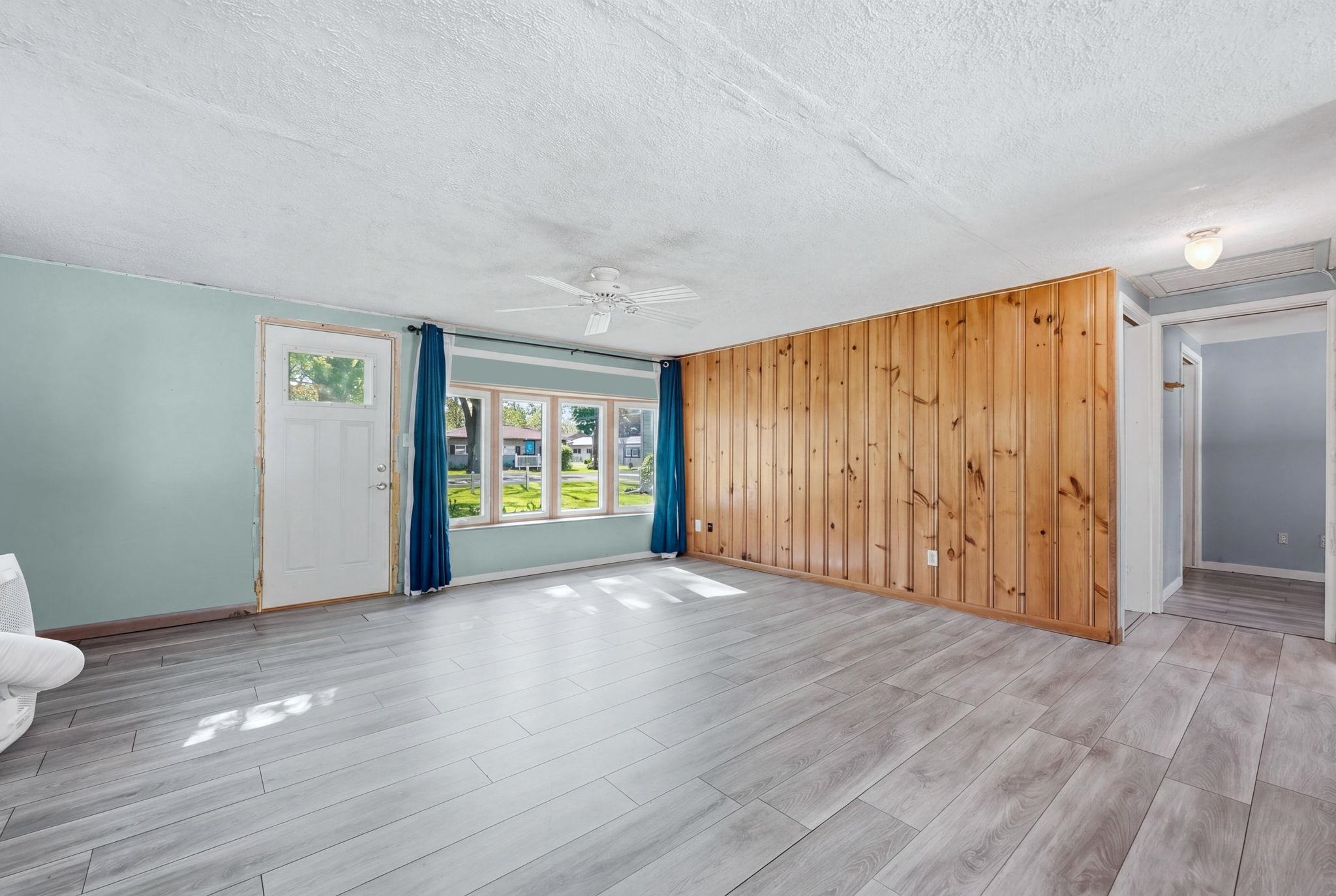 Spacious room featuring wood-finish flooring, light blue wall paint, and a natural wood panel accent wall