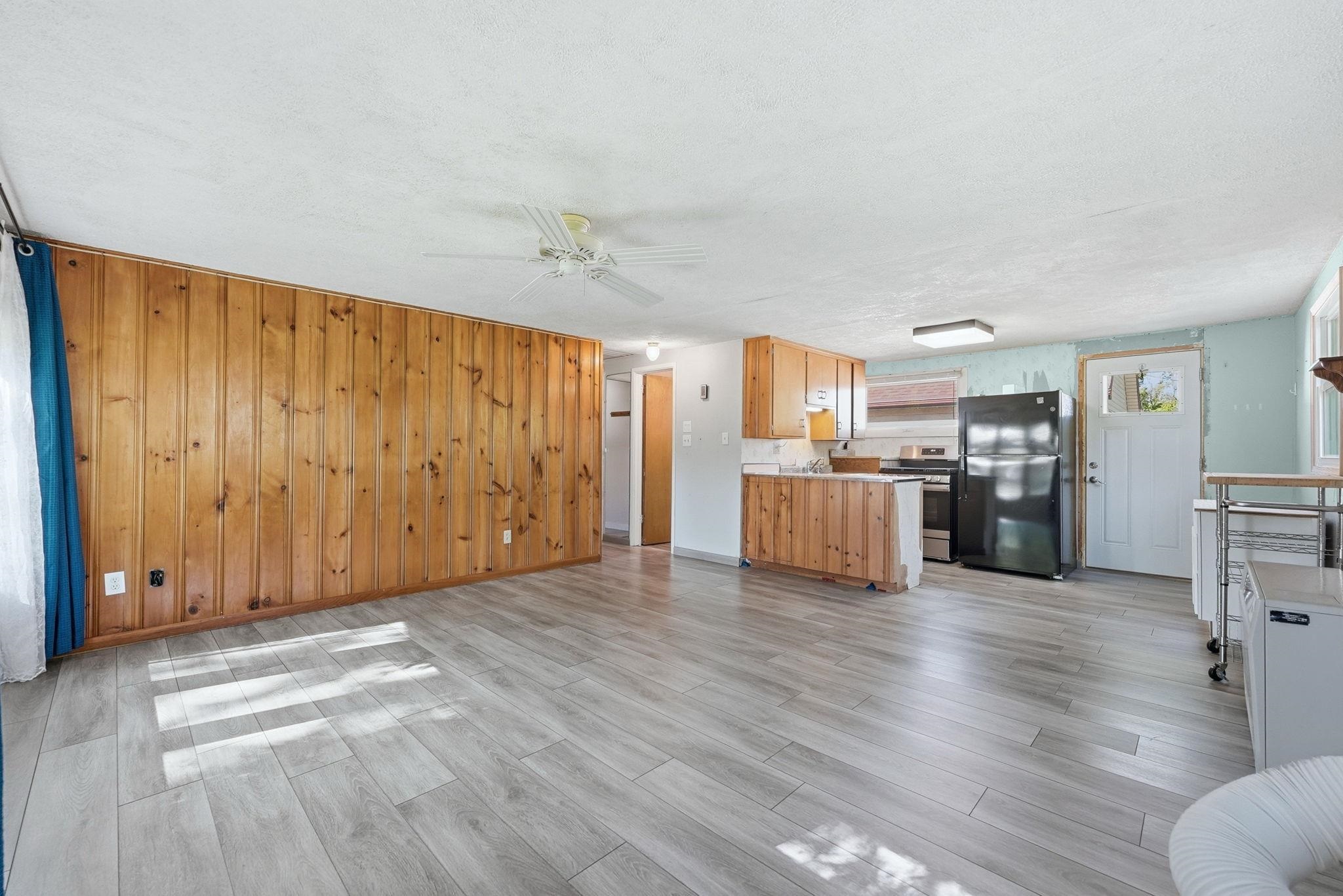 Open-concept living space featuring wood-panel accent wall, light wood-finish flooring, and a ceiling fan