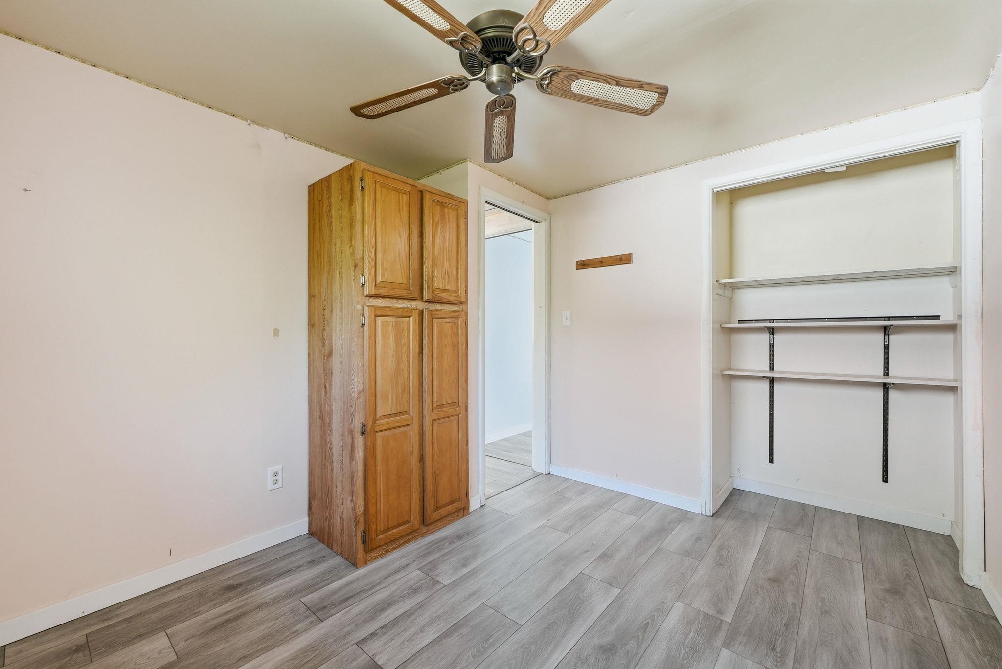 Room featuring wood-finish flooring, a built-in wooden storage cabinet, and an open closet with adjustable shelving