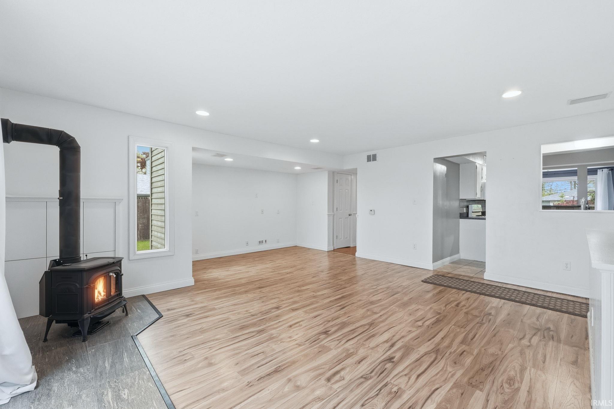 Spacious room featuring wood-finish flooring, recessed lighting, and a prominent wood-burning stove with a protective hearth