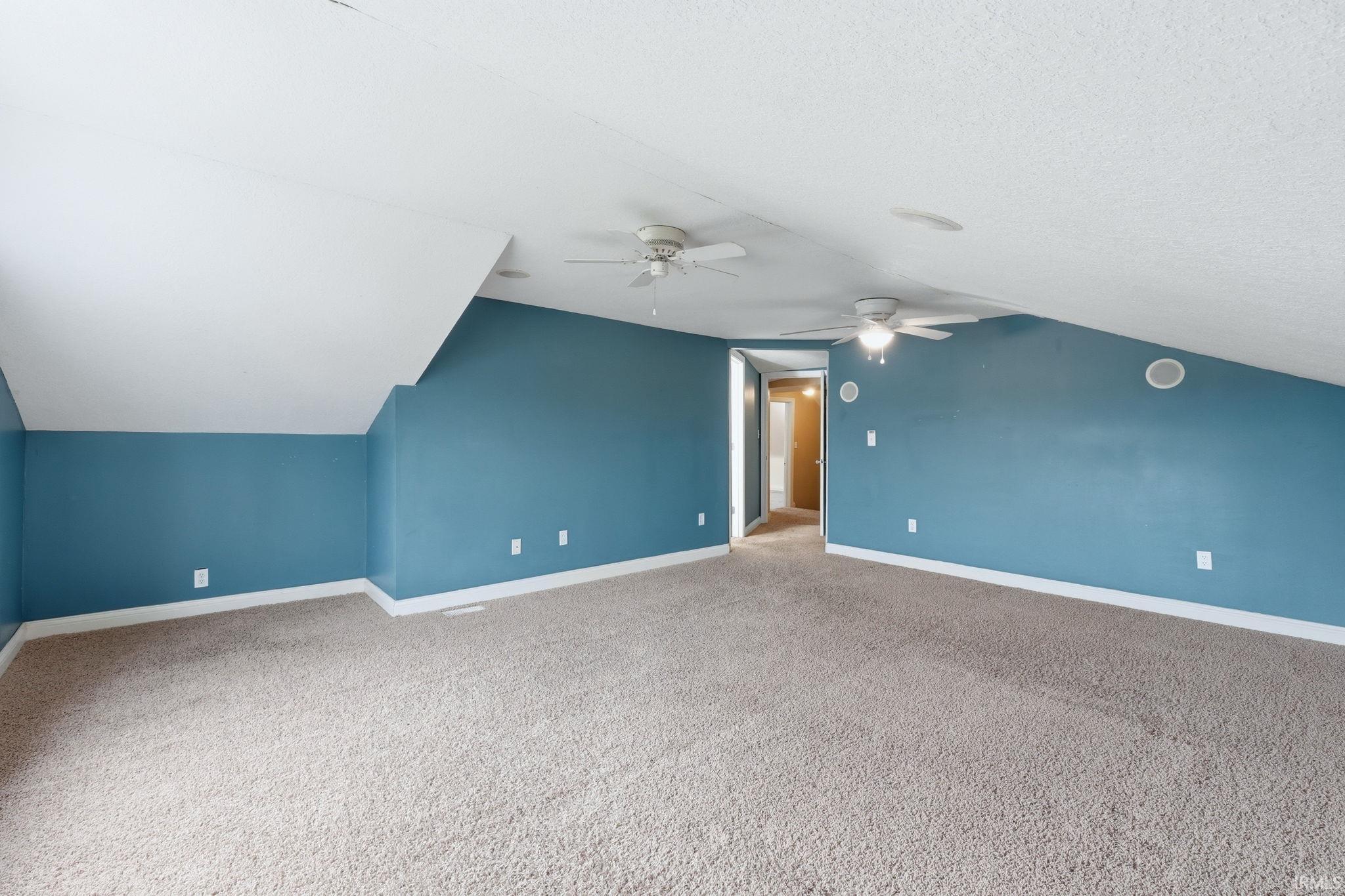 Spacious room featuring sloped ceilings, two ceiling fans, wall-to-wall carpeting, and baseboard trim