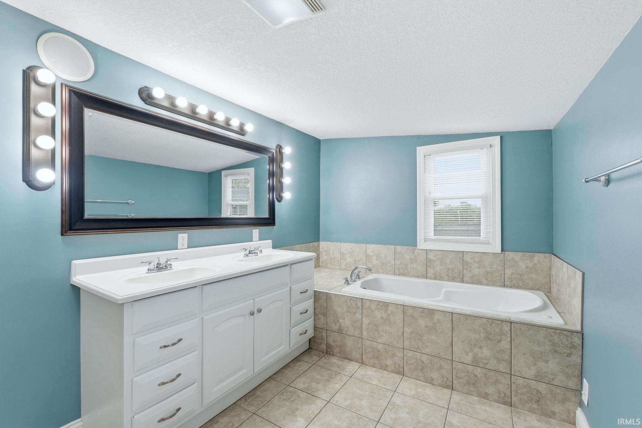 Bathroom featuring a dual vanity with white cabinetry and integrated sinks, a large framed mirror, and extensive lighting