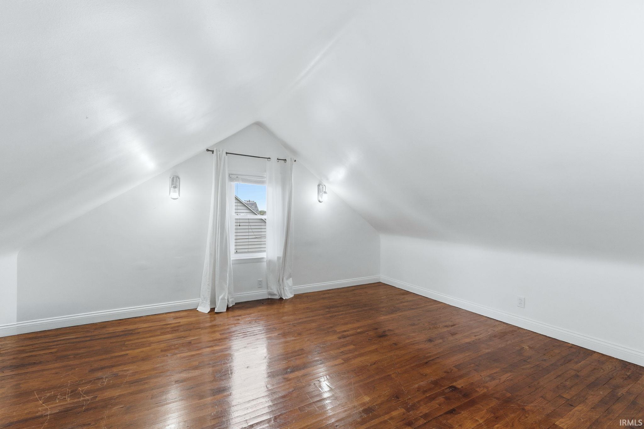 Room featuring wood-finish flooring, white walls, and a window with white curtains