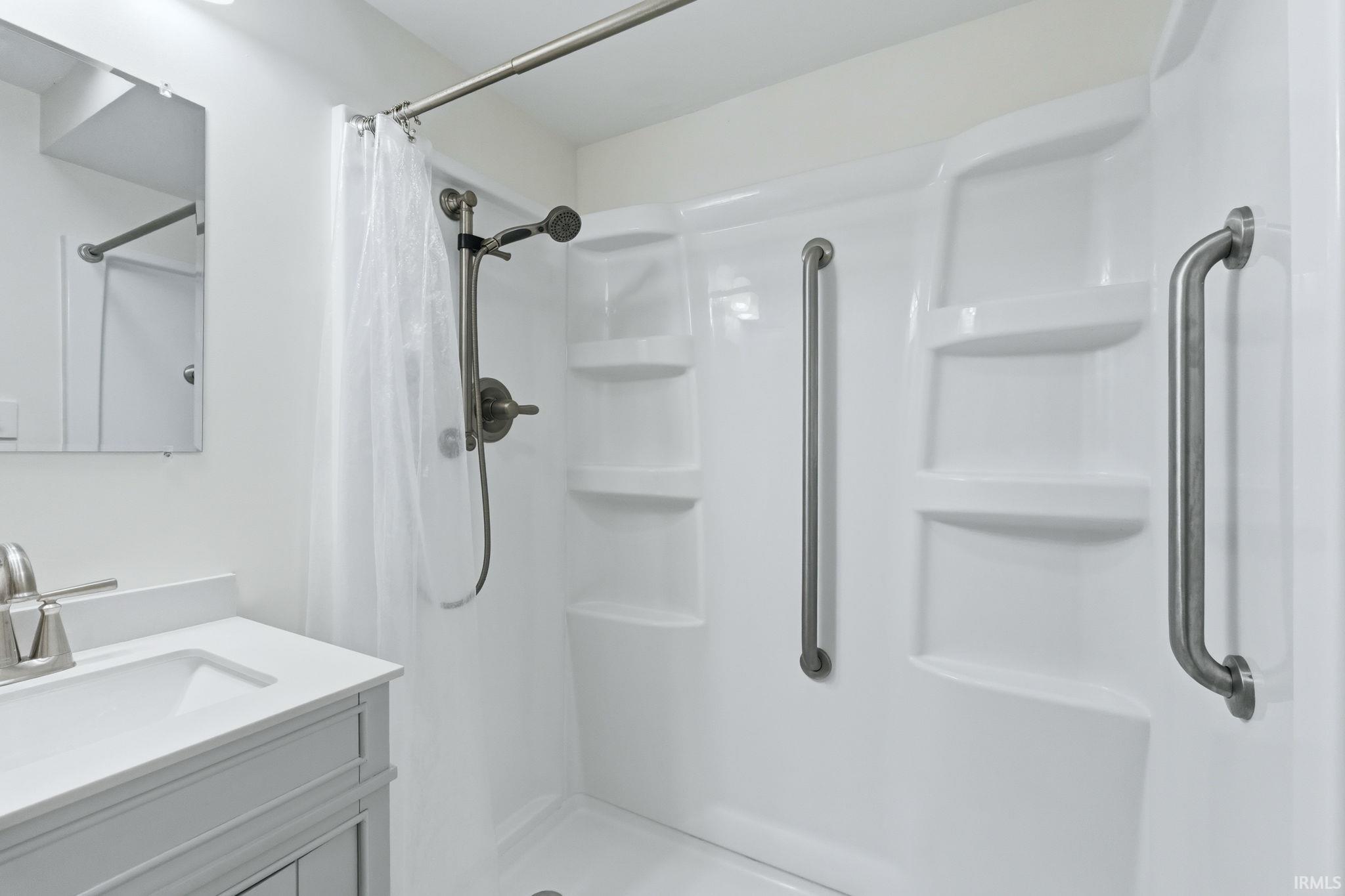 Bathroom featuring a white shower stall with built-in shelving, two grab bars, and a brushed nickel shower fixture