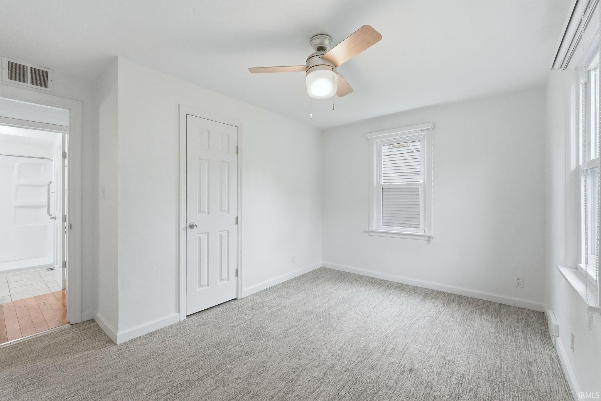 Room featuring light-toned carpeting, white walls, and a ceiling fan with integrated lighting