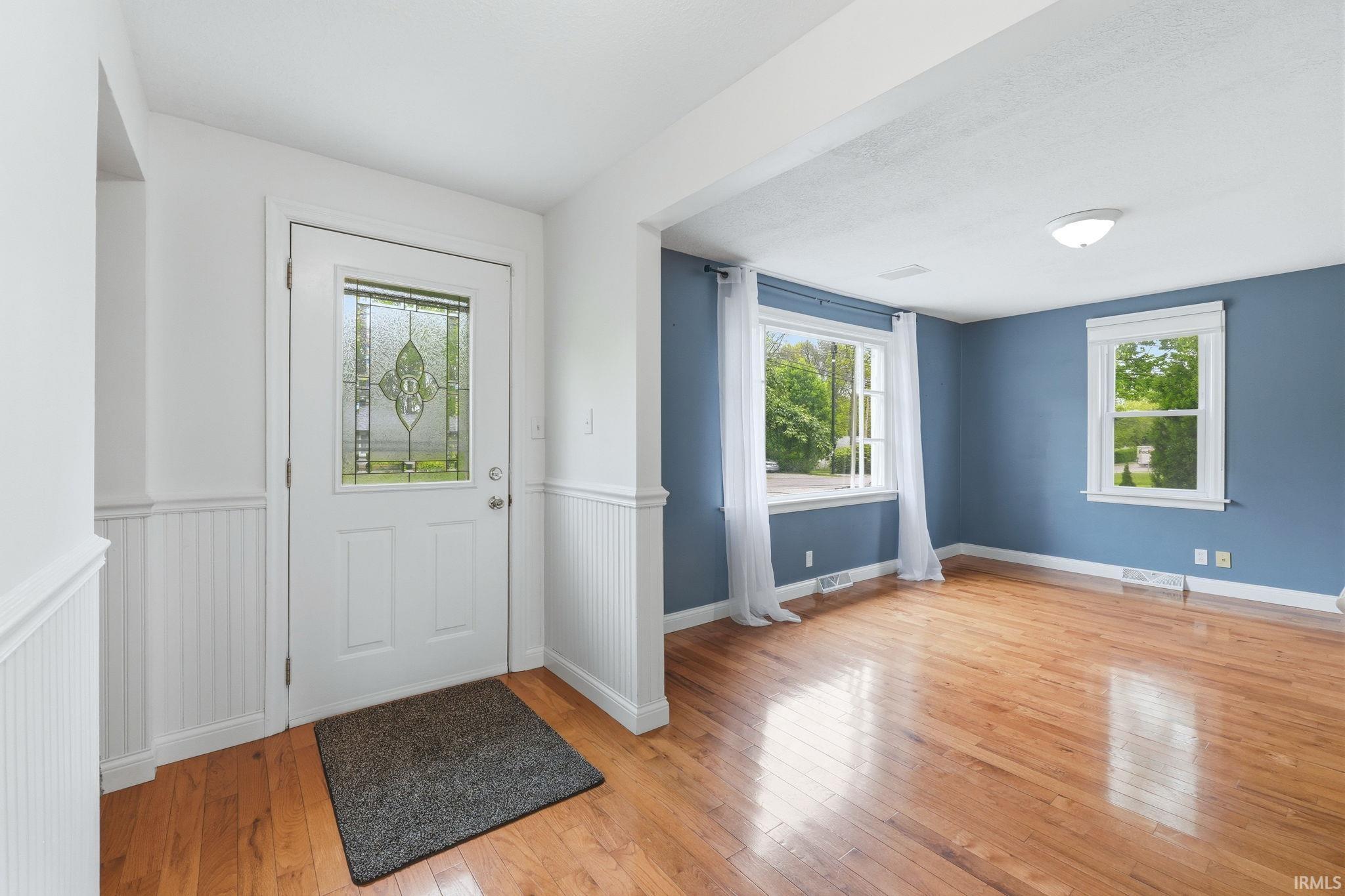 Entryway featuring a decorative glass panel door, beadboard wainscoting, and wood-finish flooring extending into the adjacent room with two windows