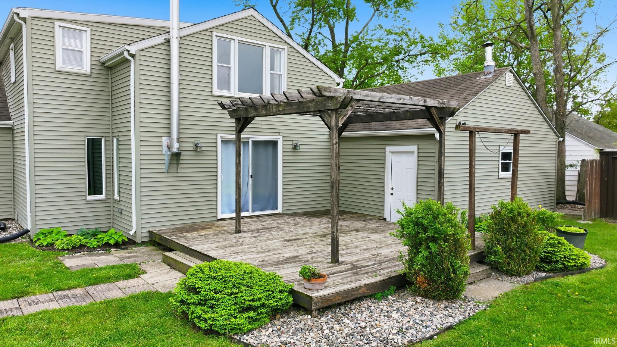 Expansive backyard deck featuring a wooden pergola, leading to a sliding glass door entry