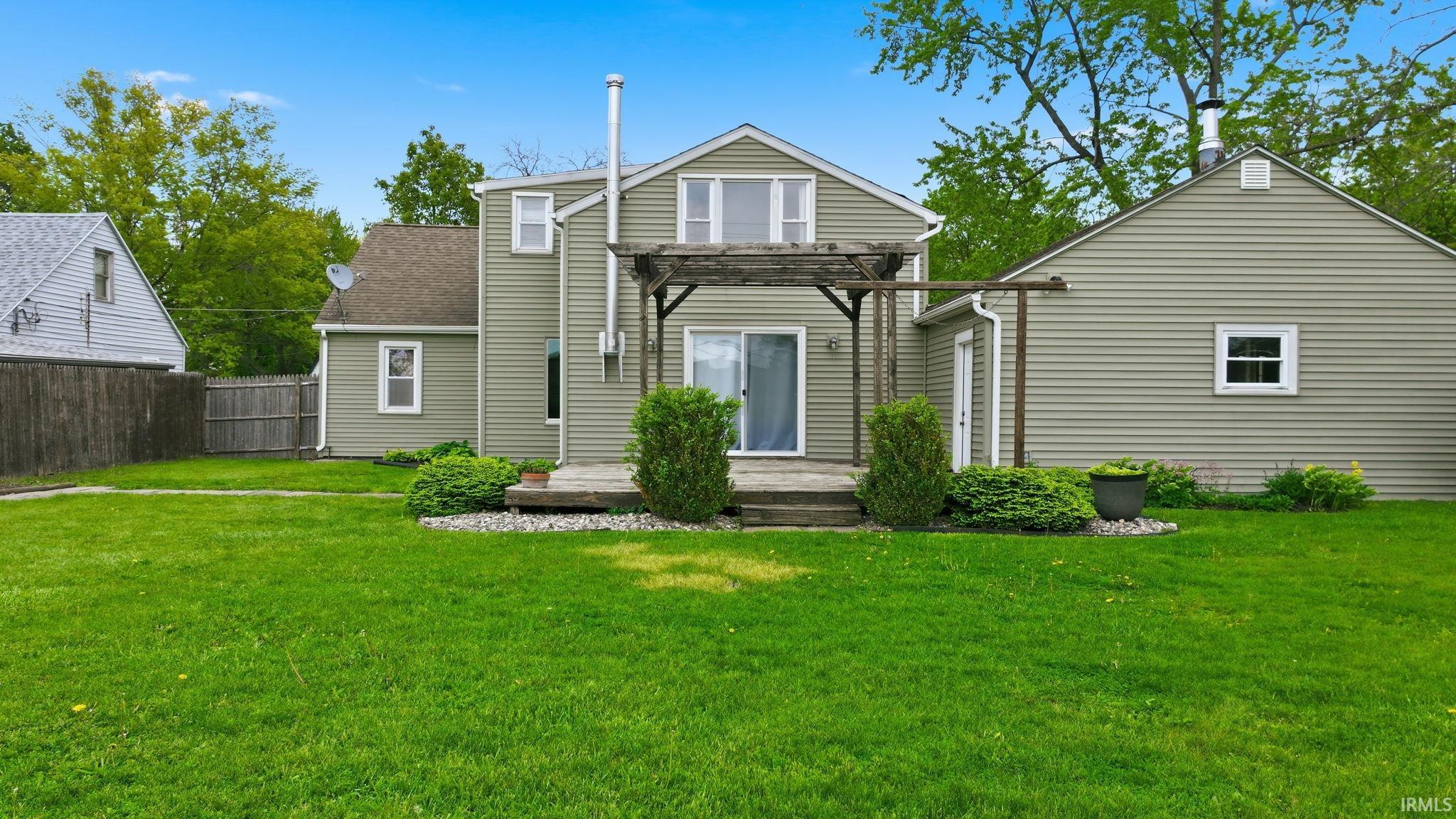 Expansive green lawn with a wooden privacy fence, a wooden deck with a pergola, and mature landscaping