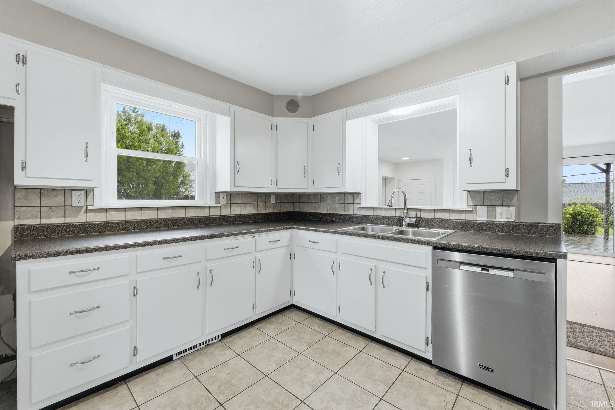 Kitchen featuring white cabinetry, dark countertops, tiled backsplash, stainless steel dishwasher, and tile flooring