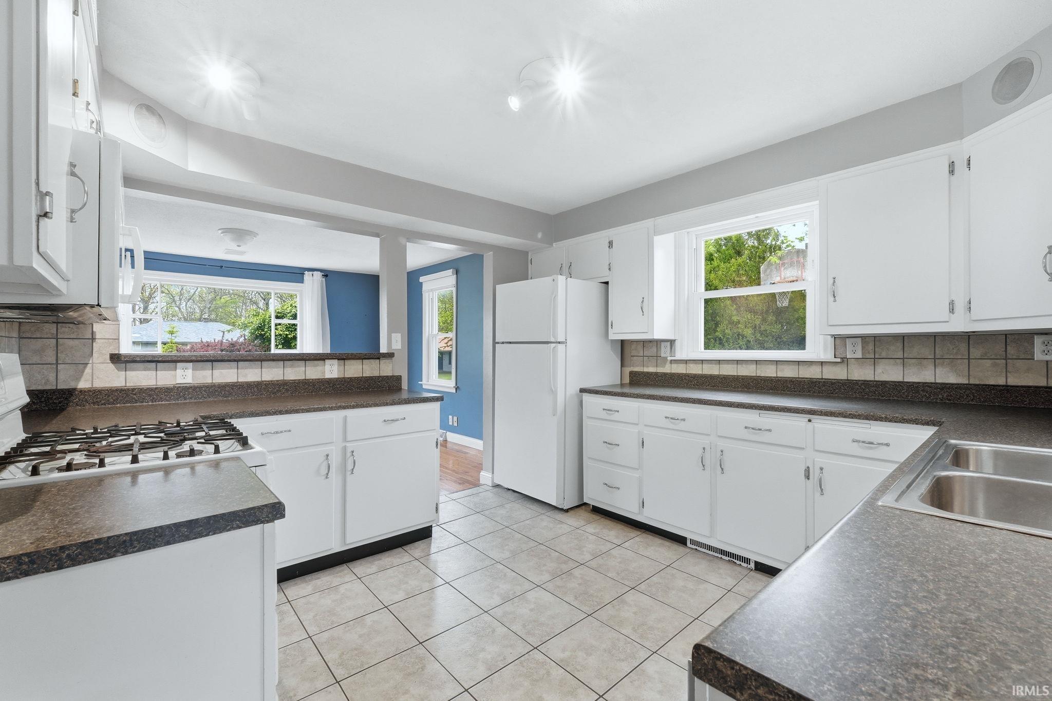 Kitchen with white cabinetry, dark speckled countertops, and a full tile backsplash