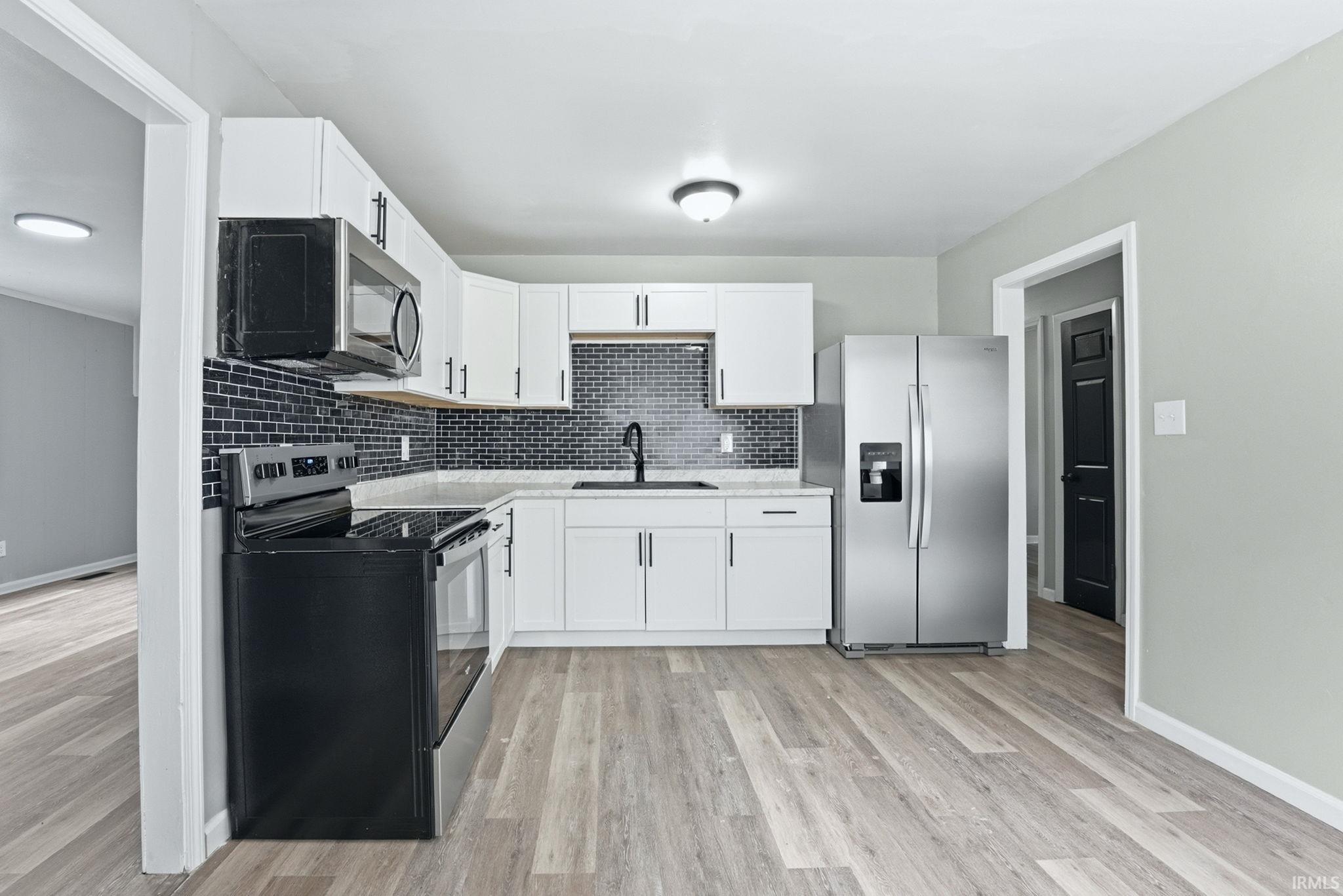 Modern kitchen featuring white cabinetry with brushed nickel hardware, a black subway tile backsplash, light-toned wood-finish flooring, and white countertops