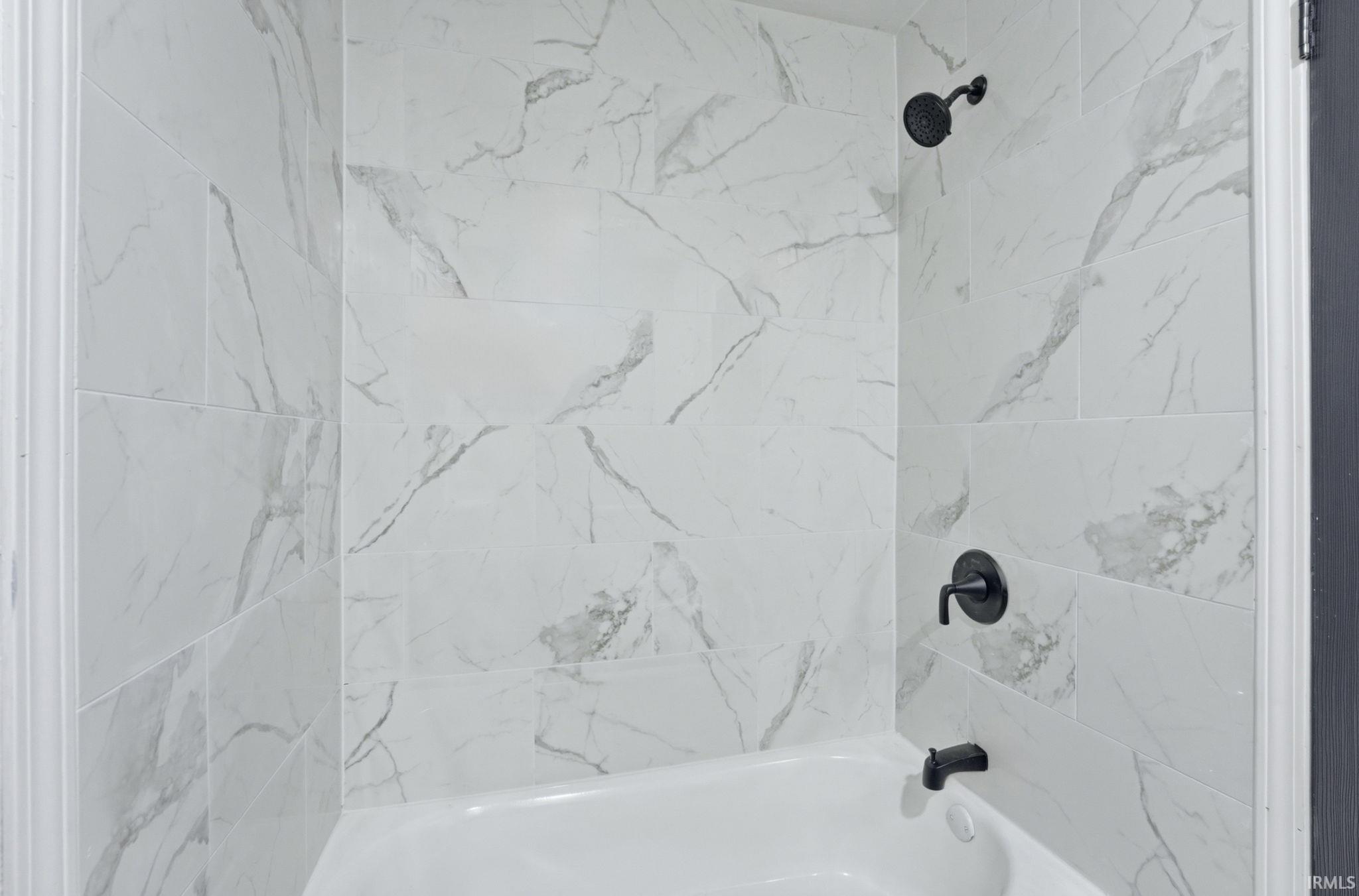 Bathtub with white subway tile surround featuring gray veining