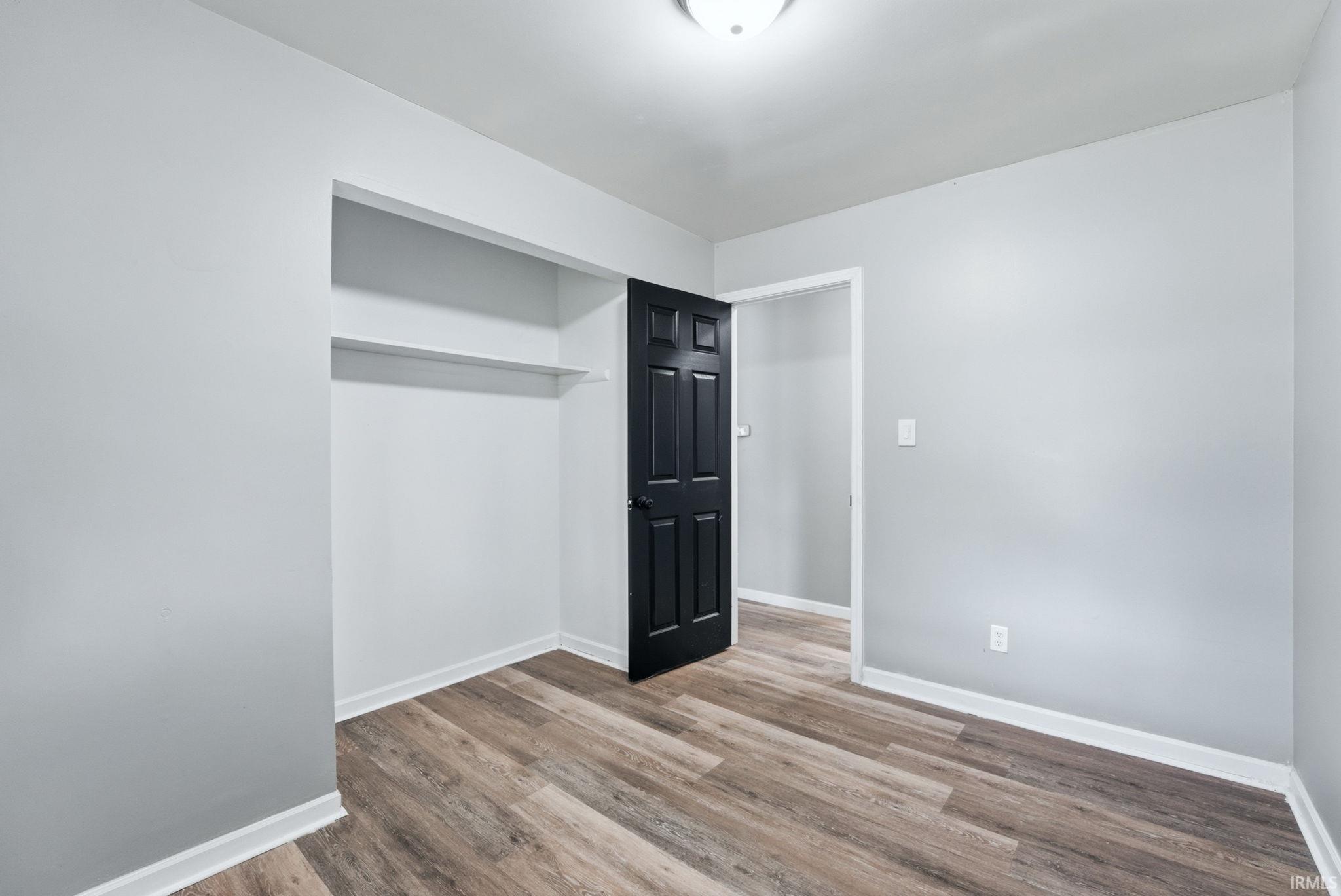Light gray painted walls, wood-finish flooring, white baseboards, a built-in closet with shelving, and a black paneled door