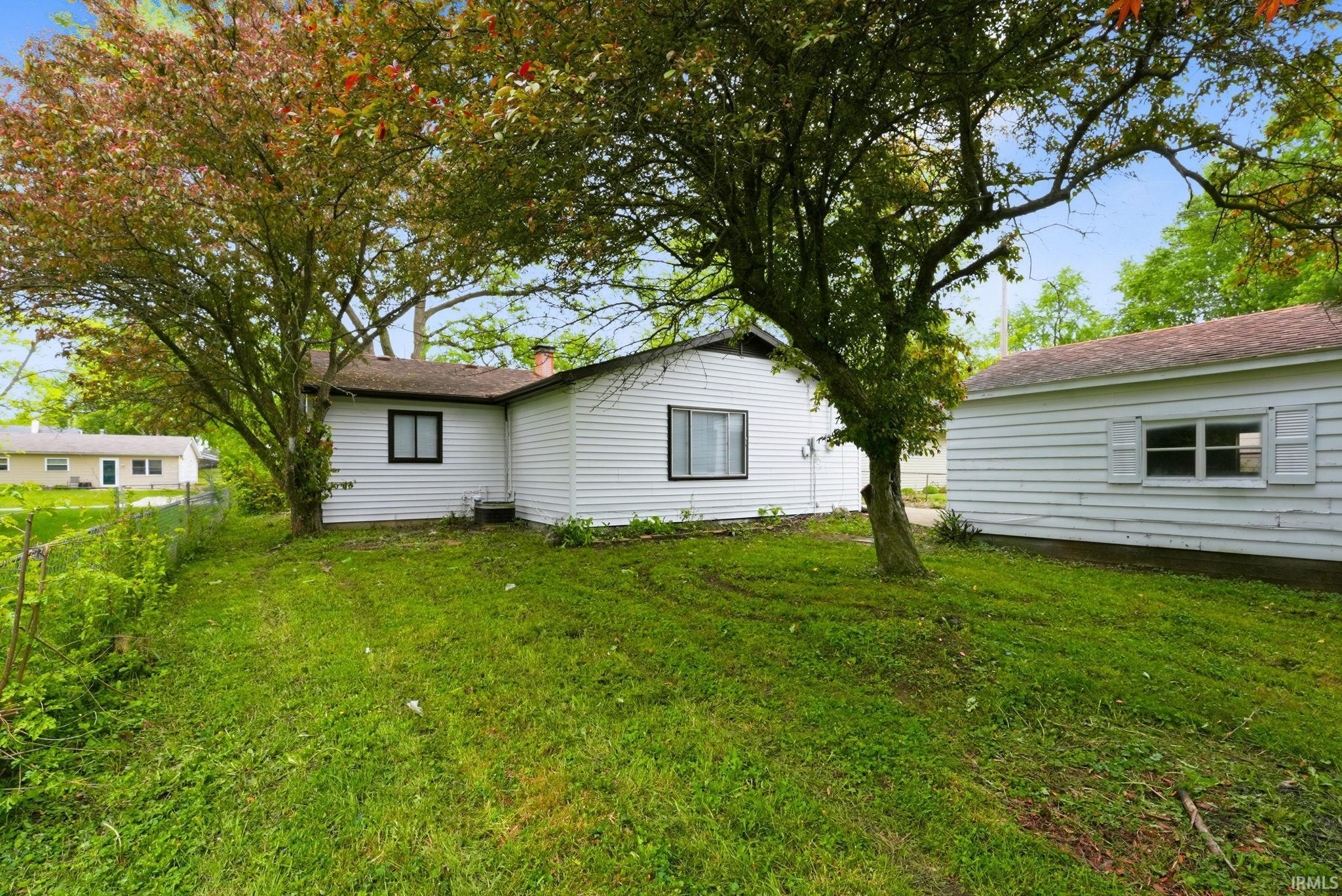 Spacious backyard featuring mature trees, a white-sided residence with dark trim windows, and a separate structure with white siding and window shutters