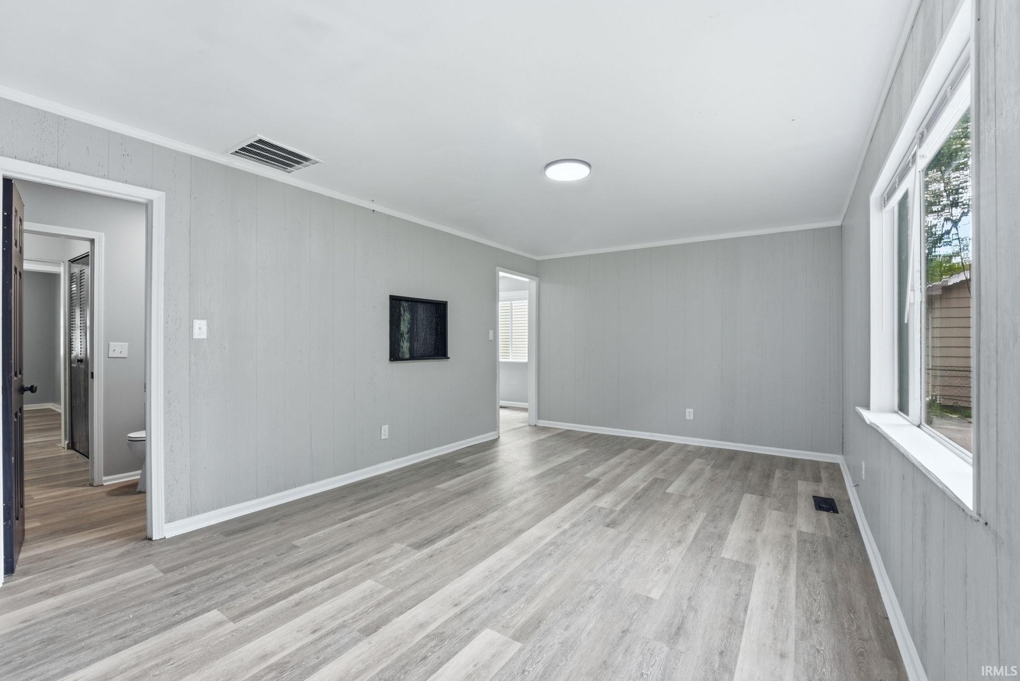 Spacious interior room featuring wood-finish flooring, light grey paneling, and white trim