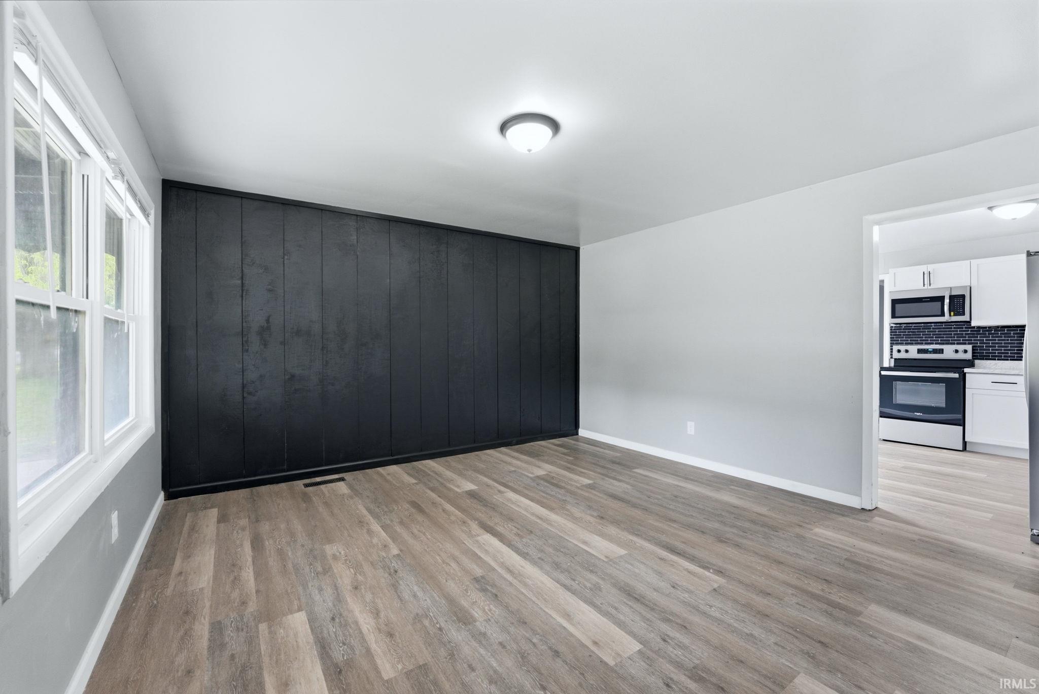 Spacious room featuring wood-finish flooring, a prominent dark accent wall with vertical paneling, and a white trim window