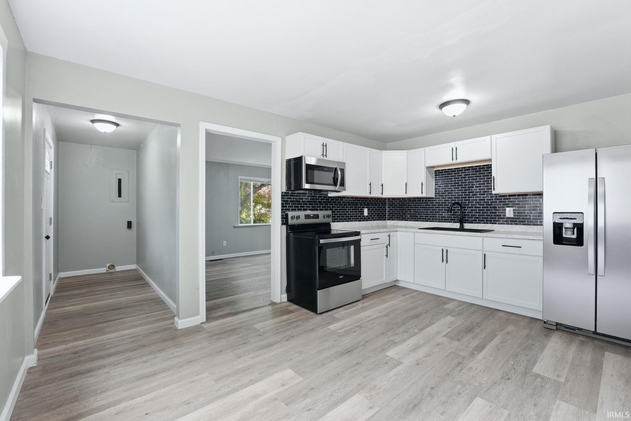Modern kitchen featuring white cabinetry, a dark subway tile backsplash, stainless steel appliances, and light wood-finish flooring