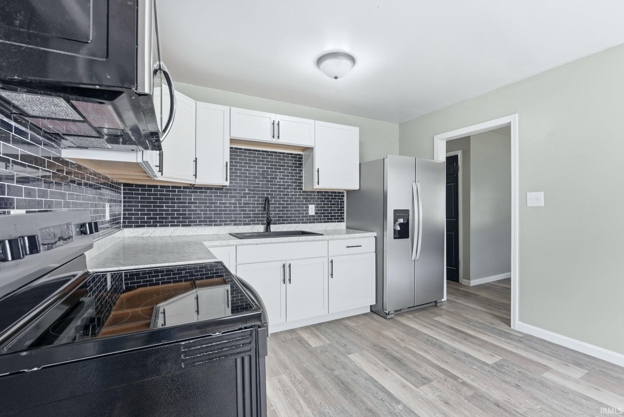 Modern kitchen featuring white cabinetry, a dark subway tile backsplash, light-toned countertops, stainless steel refrigerator, and wood-finish flooring