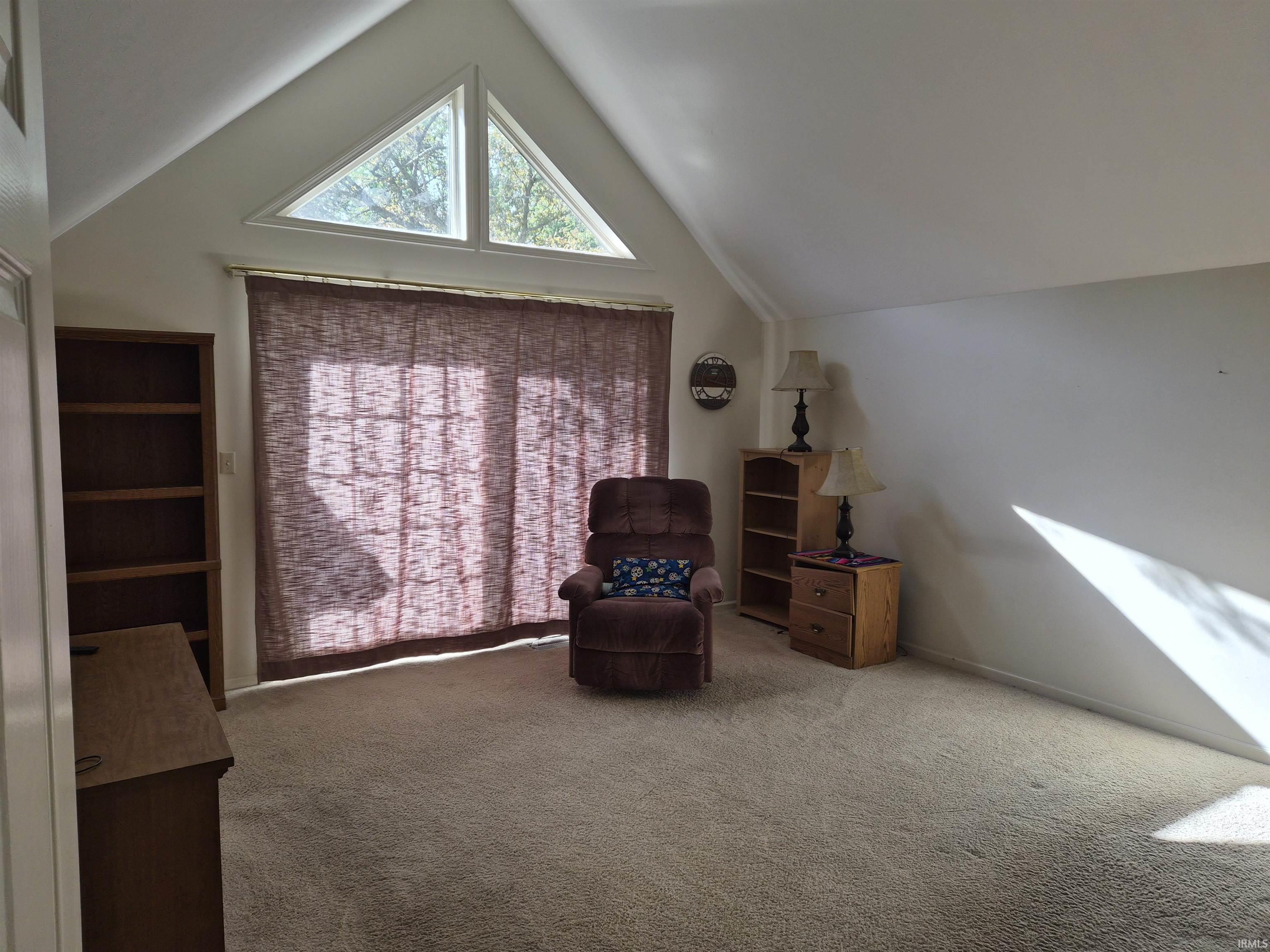 Vaulted ceiling room featuring light-toned carpeting, a large sliding glass door with privacy blinds, and triangular architectural windows