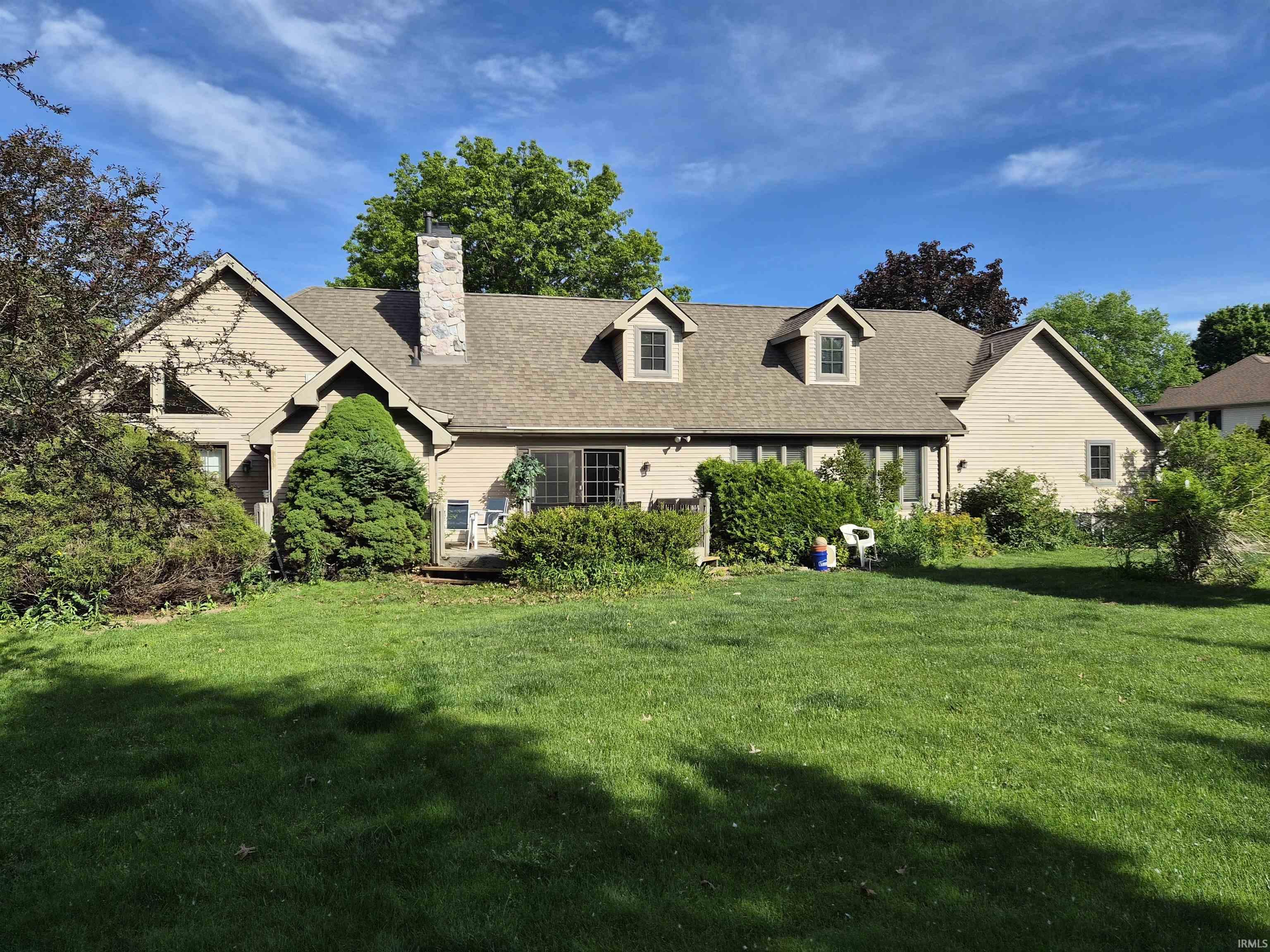 Expansive backyard featuring a manicured lawn, established landscaping, and a wood deck