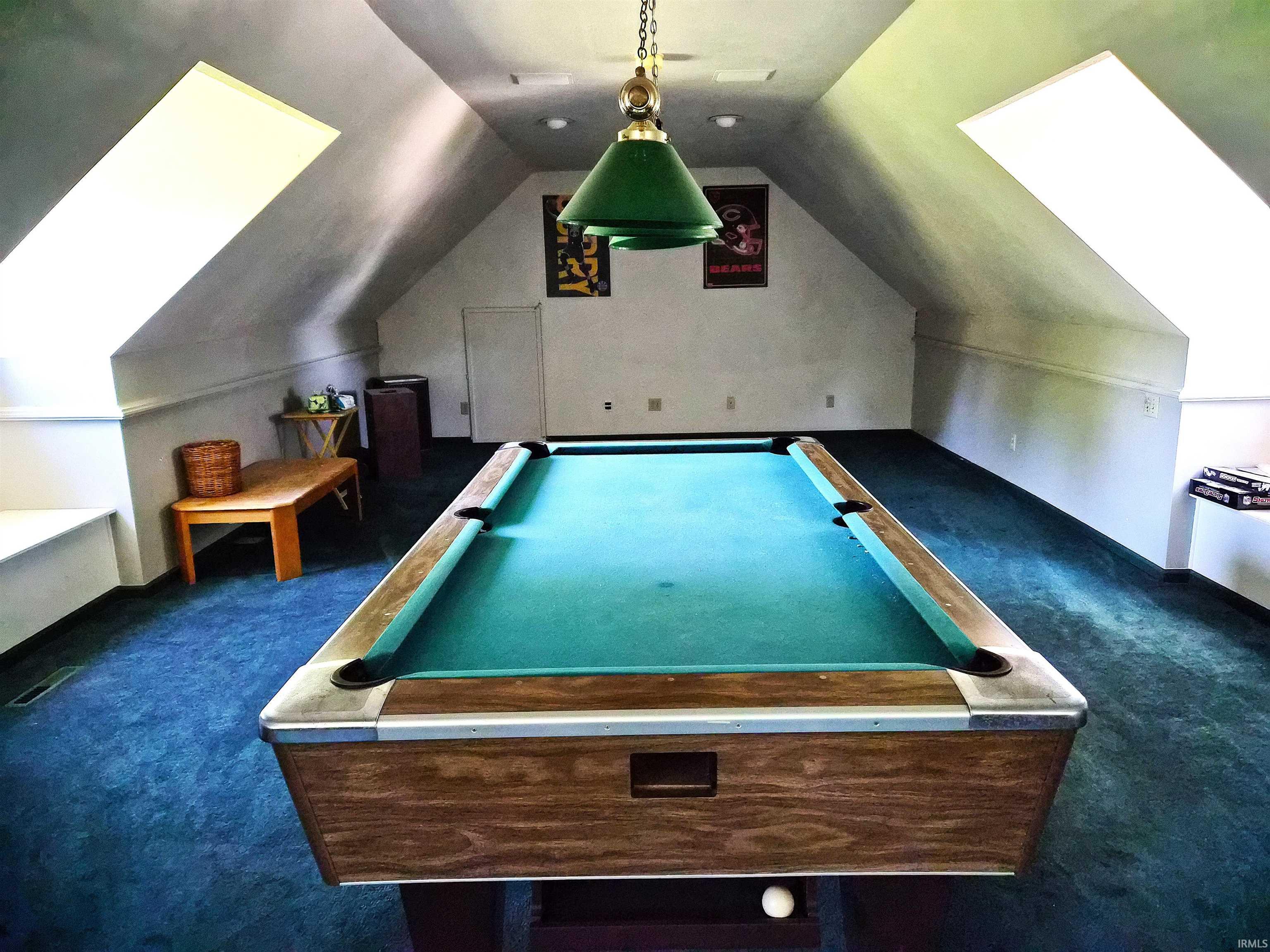 Spacious attic room featuring sloped ceilings, two large skylights, and deep blue carpeting