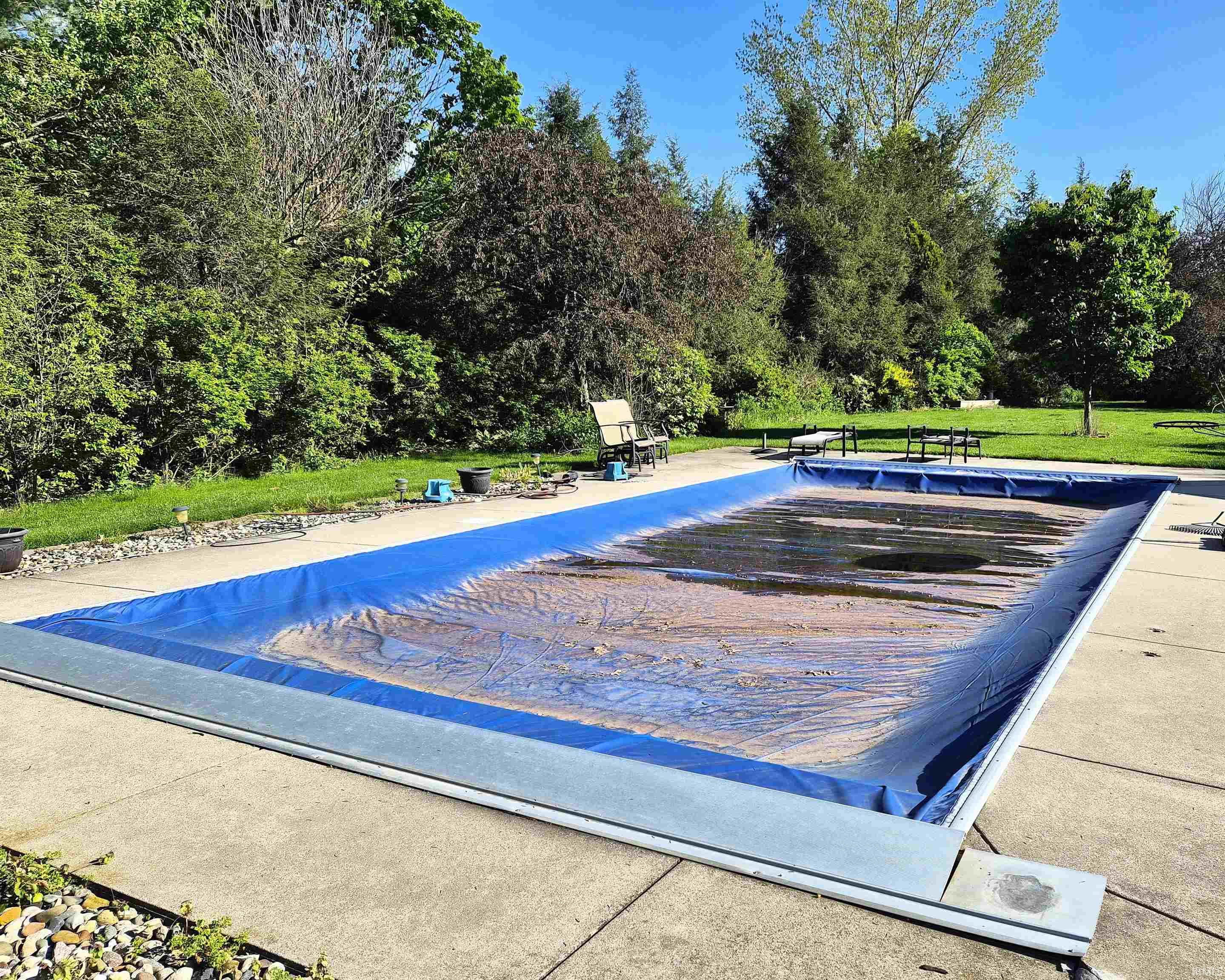 Rectangular in-ground pool with a blue safety cover, surrounded by concrete decking