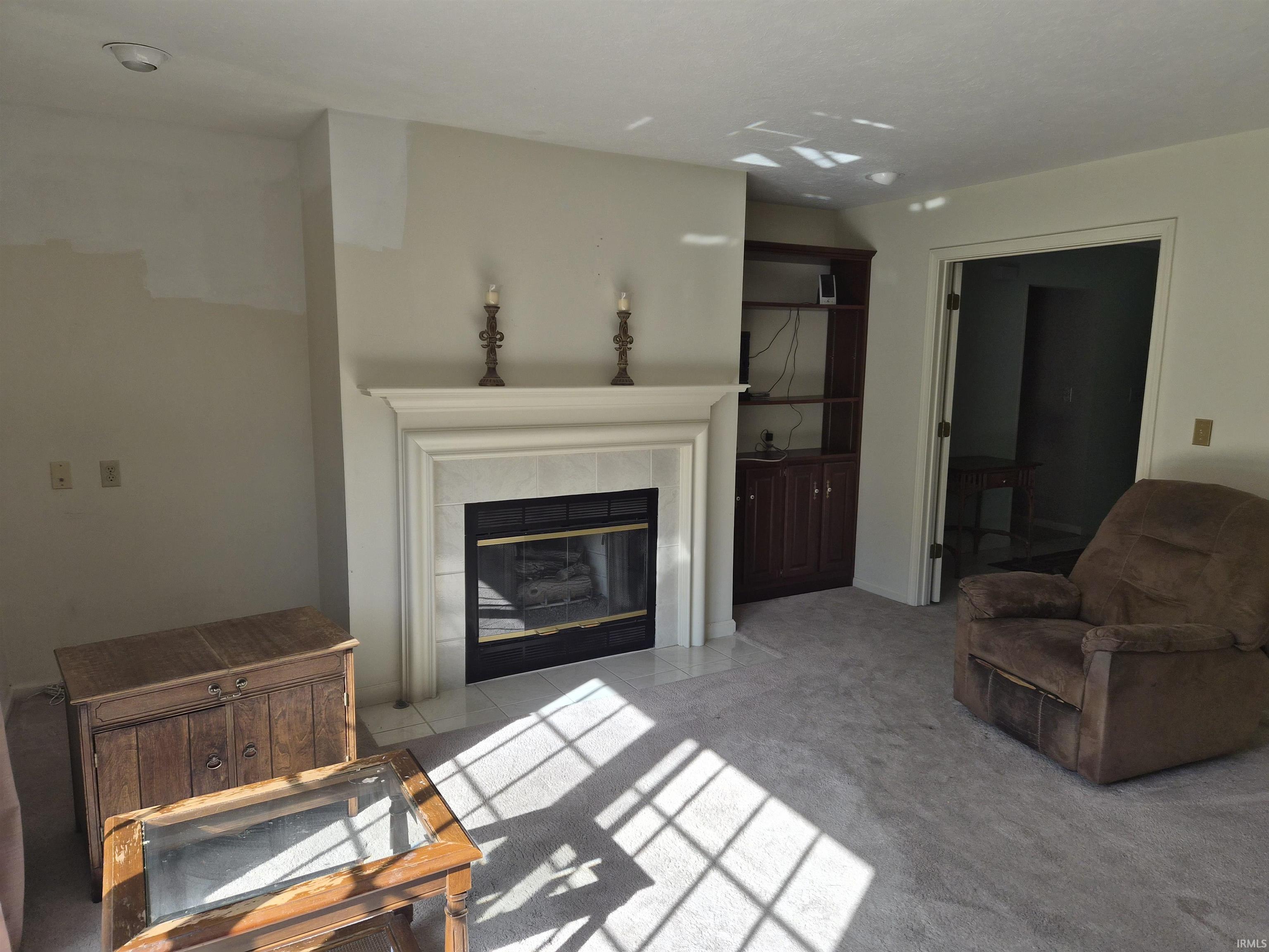 Carpeted living space featuring a fireplace with a white mantel, black firebox, and a tiled hearth