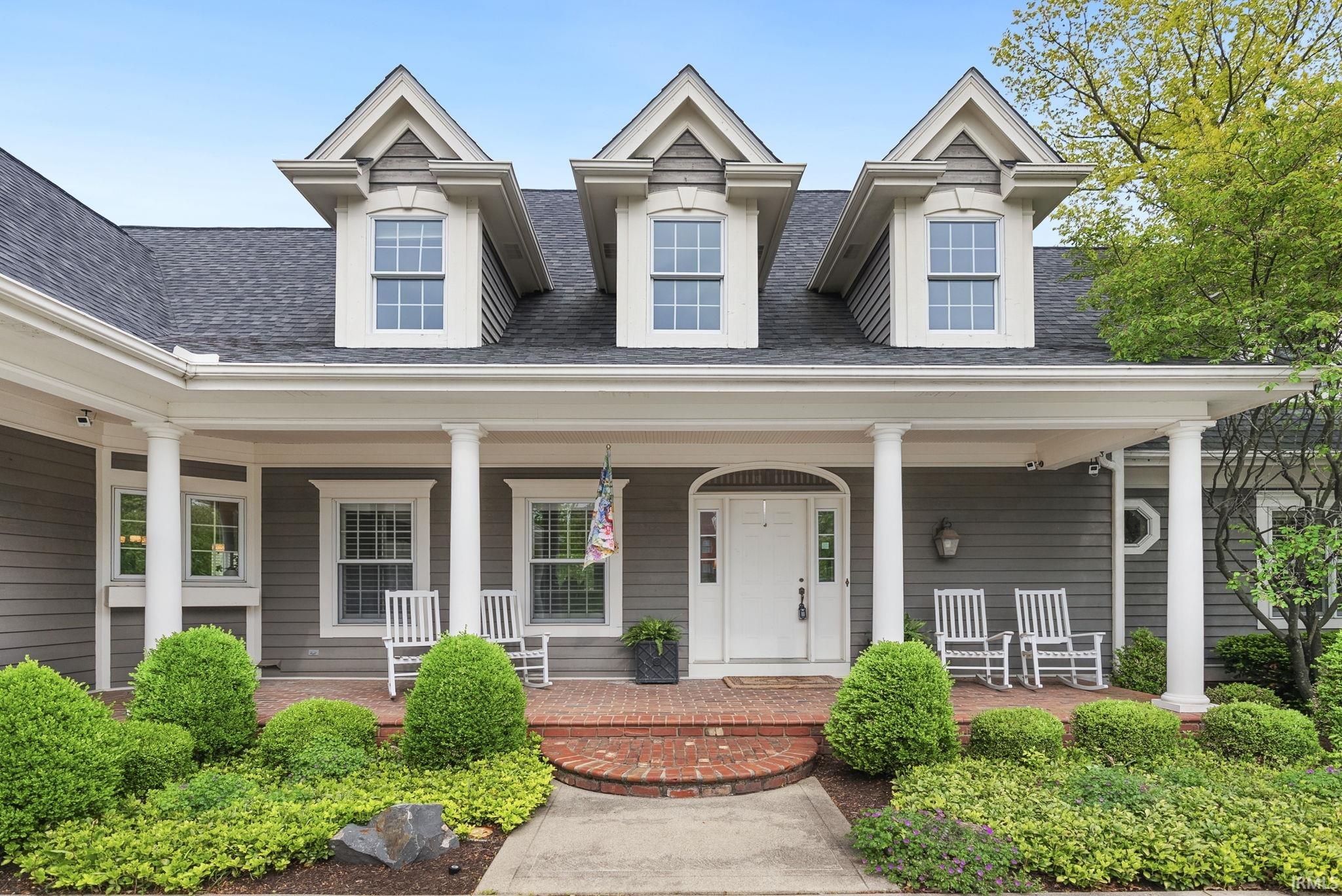 Traditional exterior featuring dormer windows, a covered front porch with white columns, and gray siding