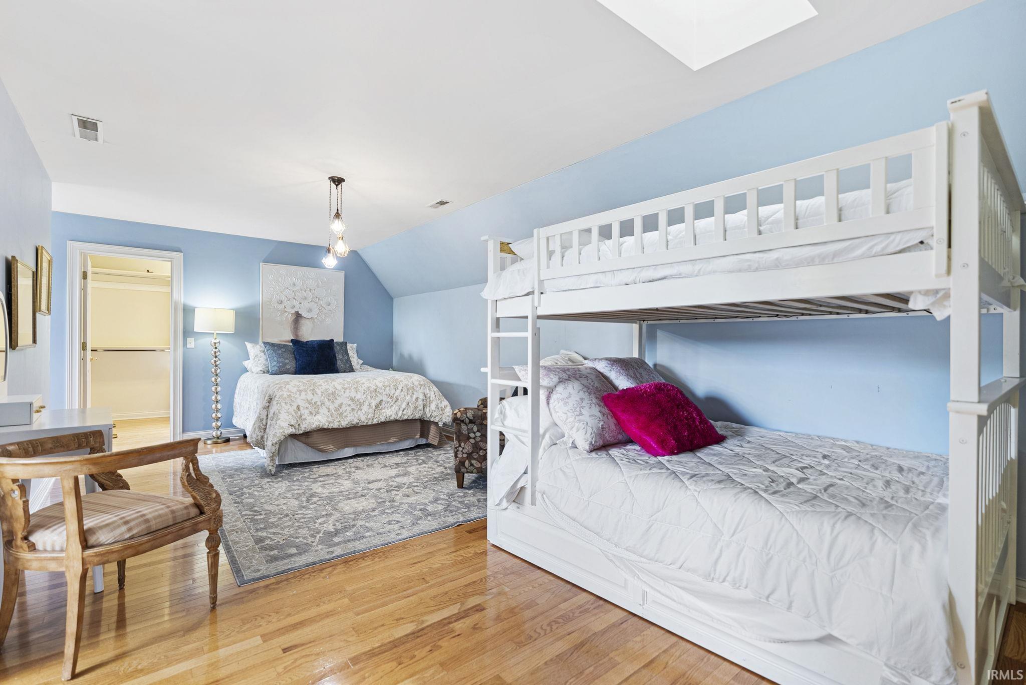 Wood-finish flooring throughout, featuring a skylight, a built-in closet with shelving, a contemporary suspended light fixture, and an attic dormer ceiling