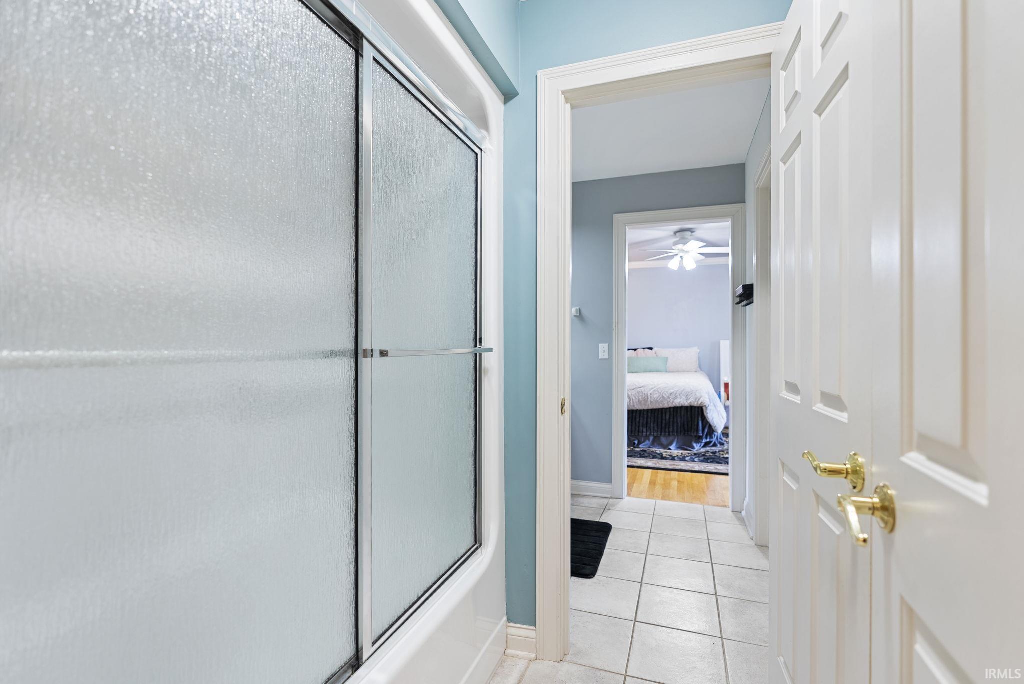 Frosted glass shower enclosure with sliding panels, tile flooring, and white paneled interior doors with brass hardware