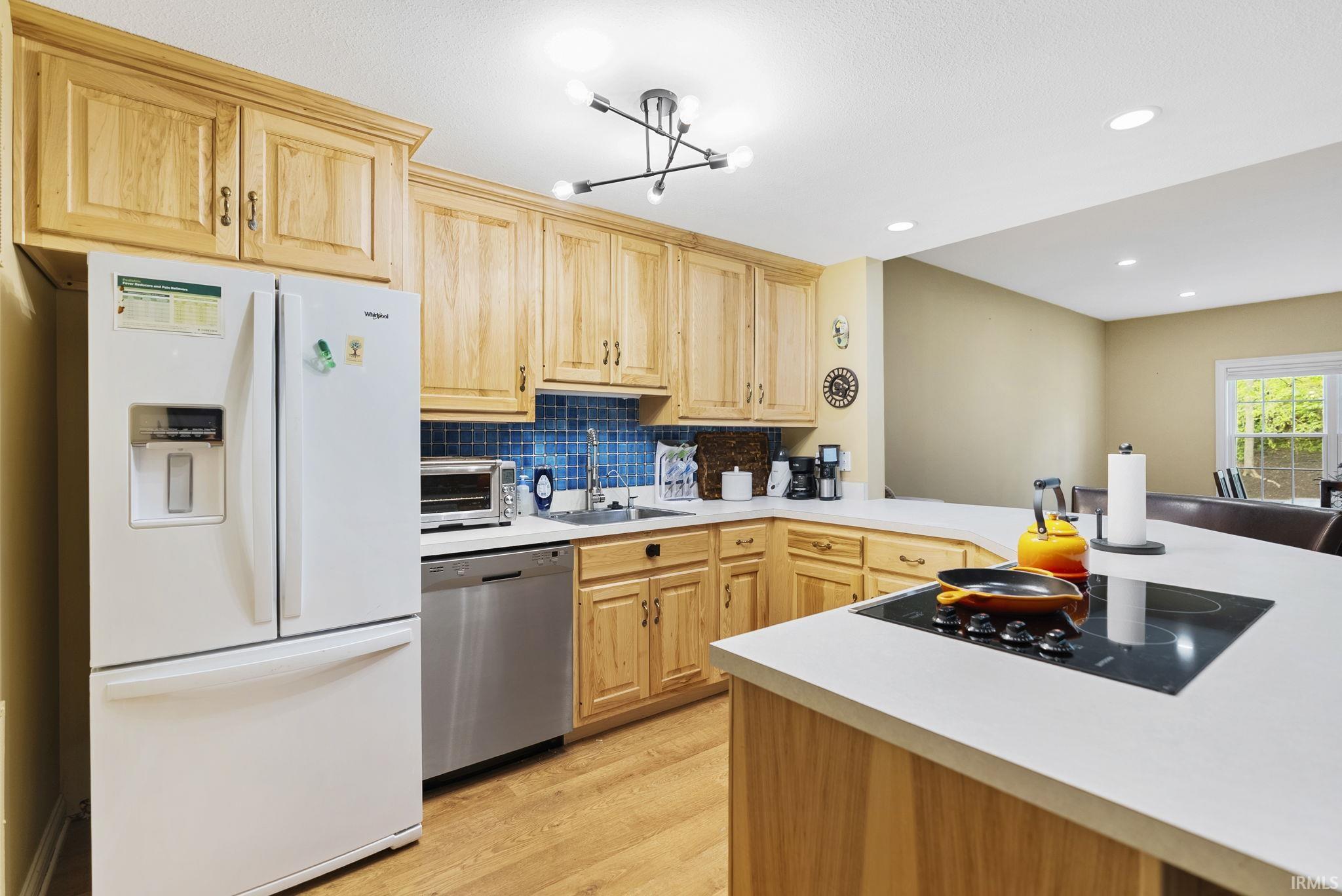 Modern kitchen featuring light wood cabinetry, a tile backsplash, light countertops, and wood-finish flooring