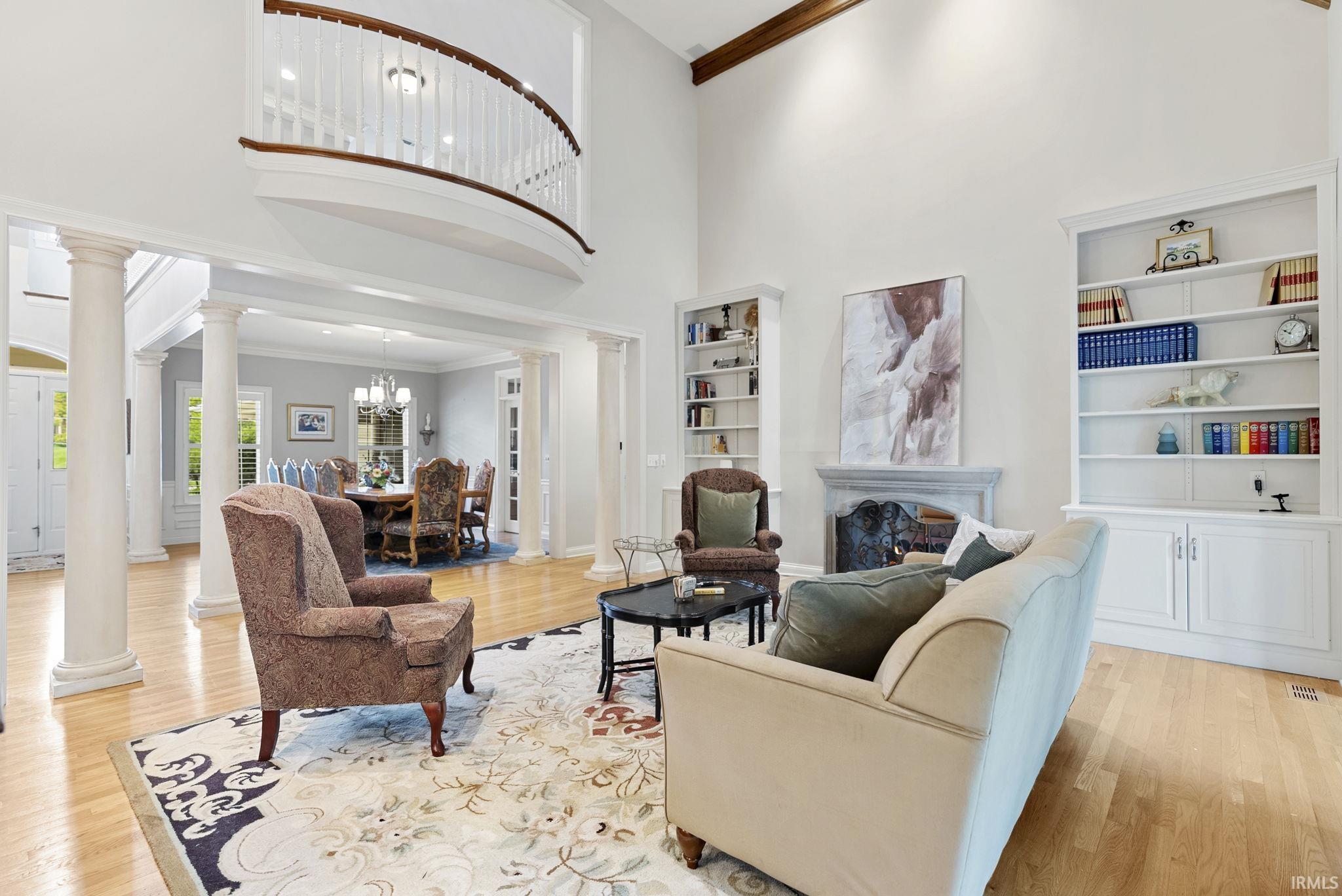 Spacious living room featuring a double-height ceiling, hardwood flooring, a stone fireplace, and built-in shelving